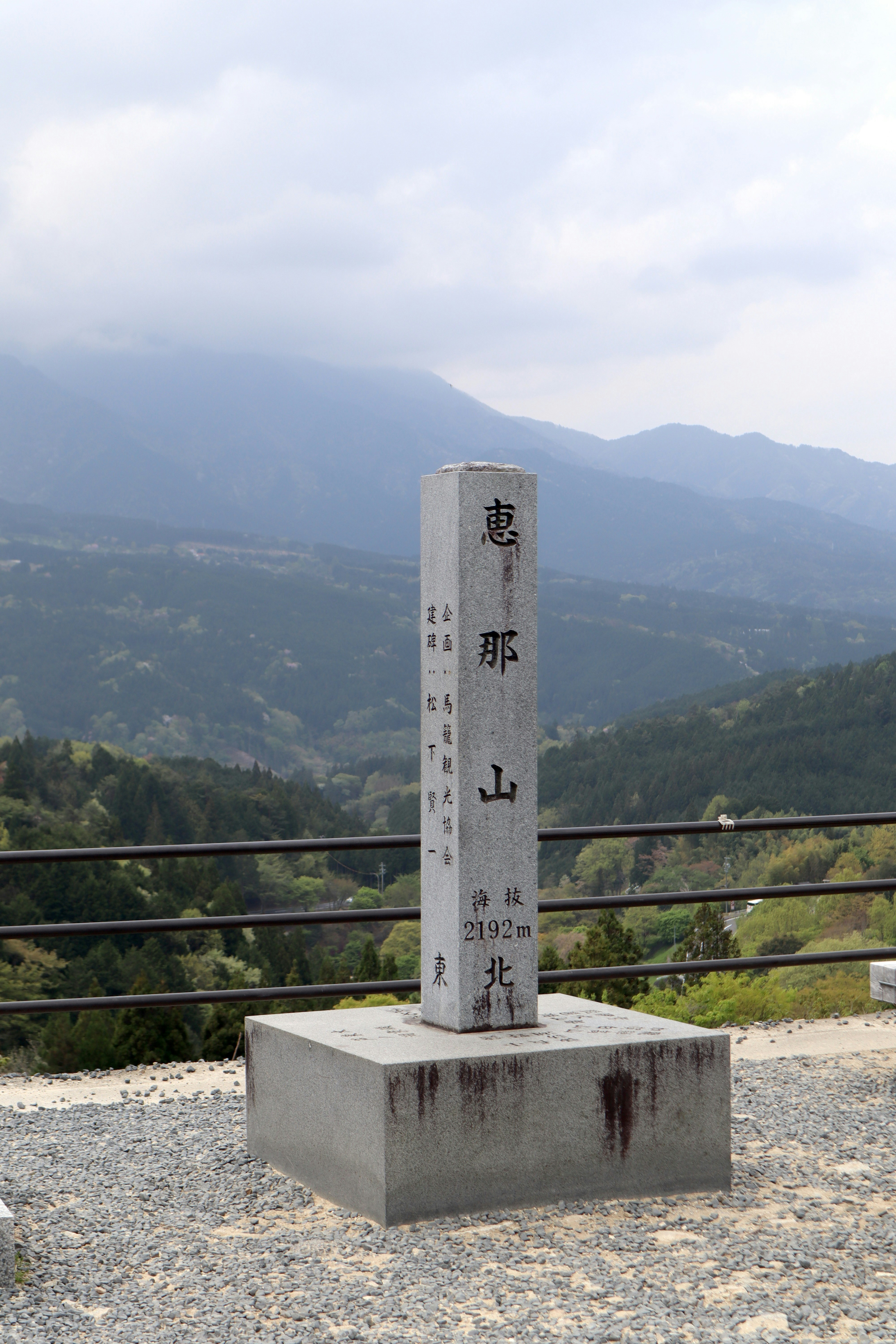 Monumento de piedra con texto japonés y vistas a la montaña.