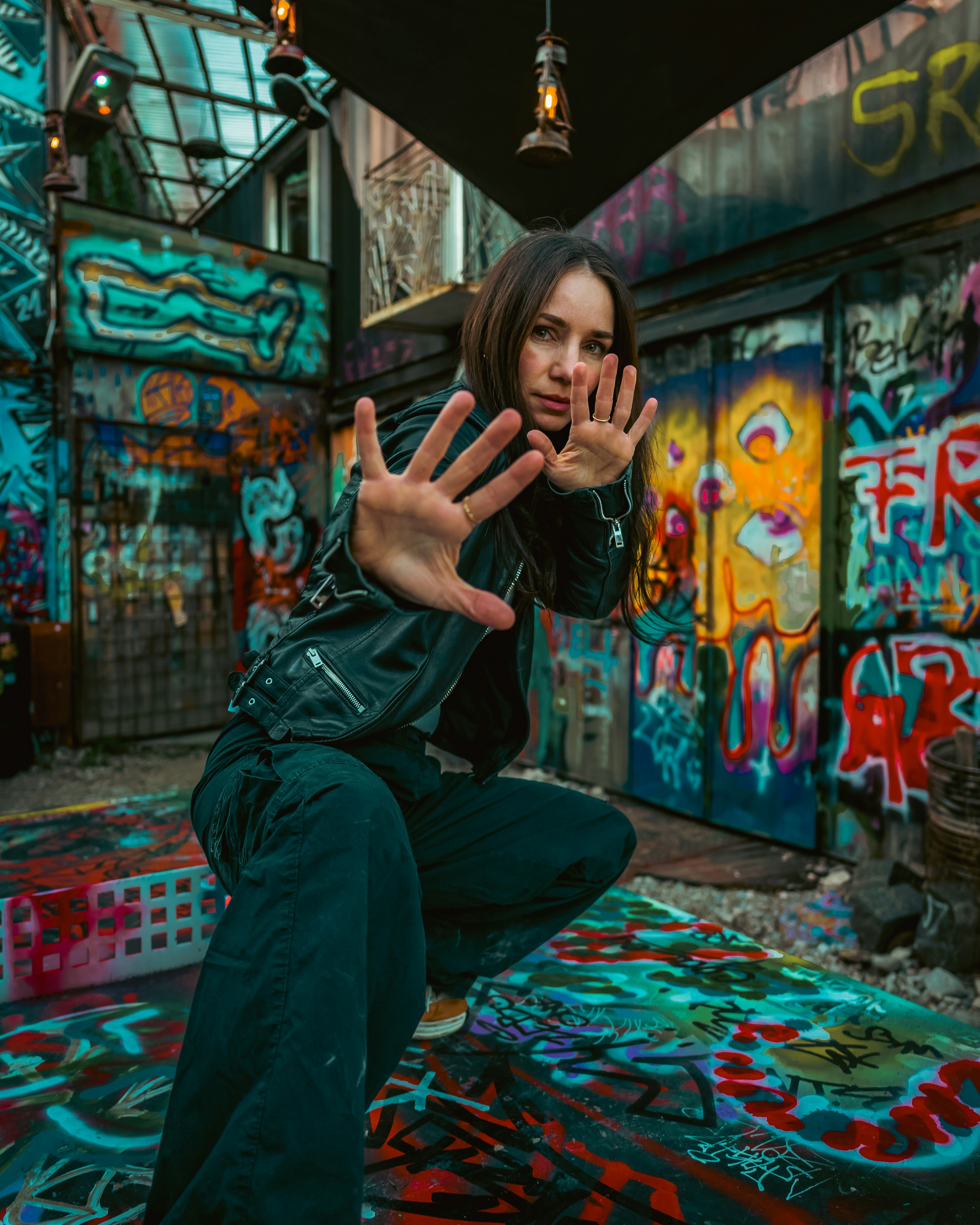 Wanita berjaket kulit berpose di gang yang tertutup grafiti.