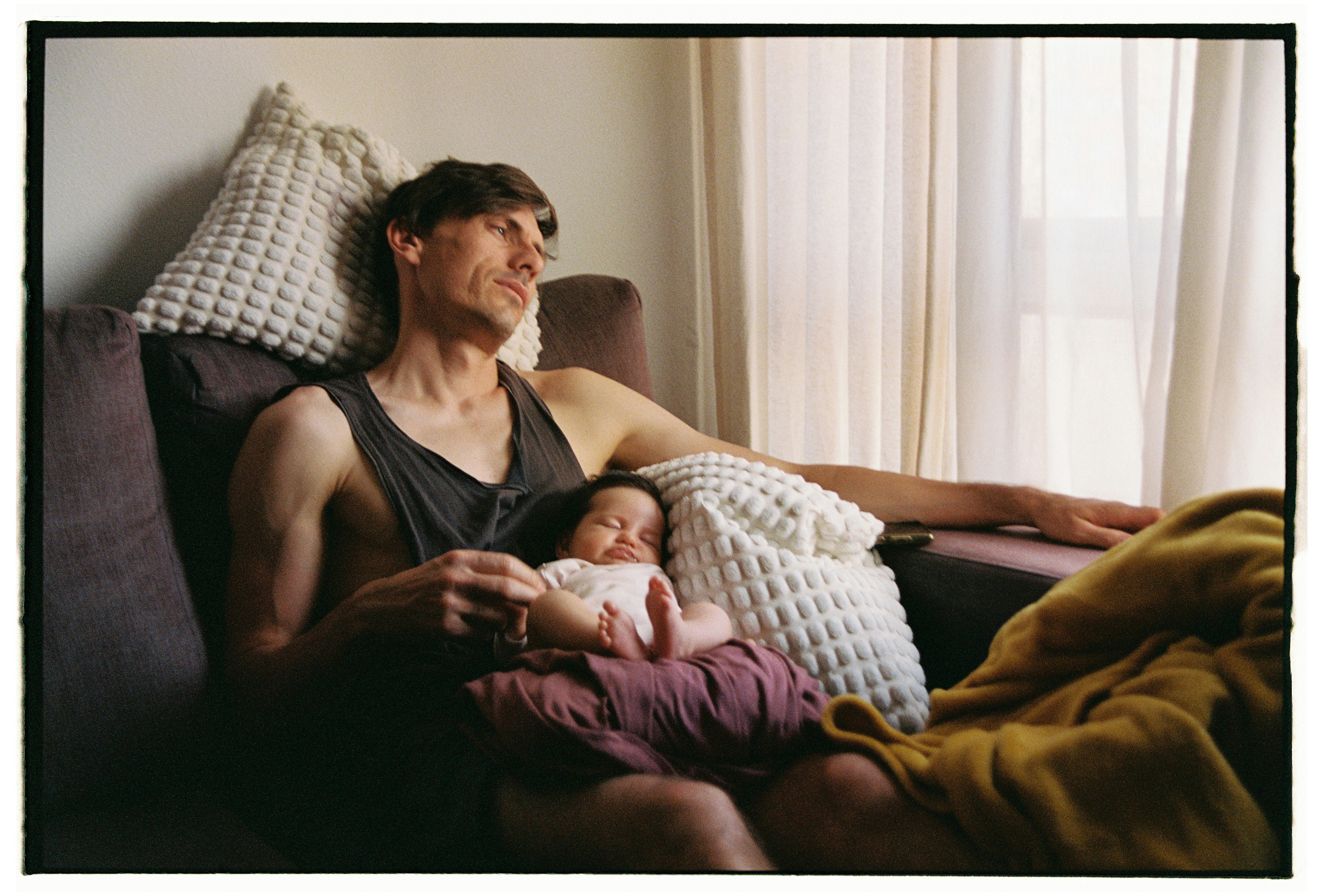 Man holding a sleeping baby on a couch.