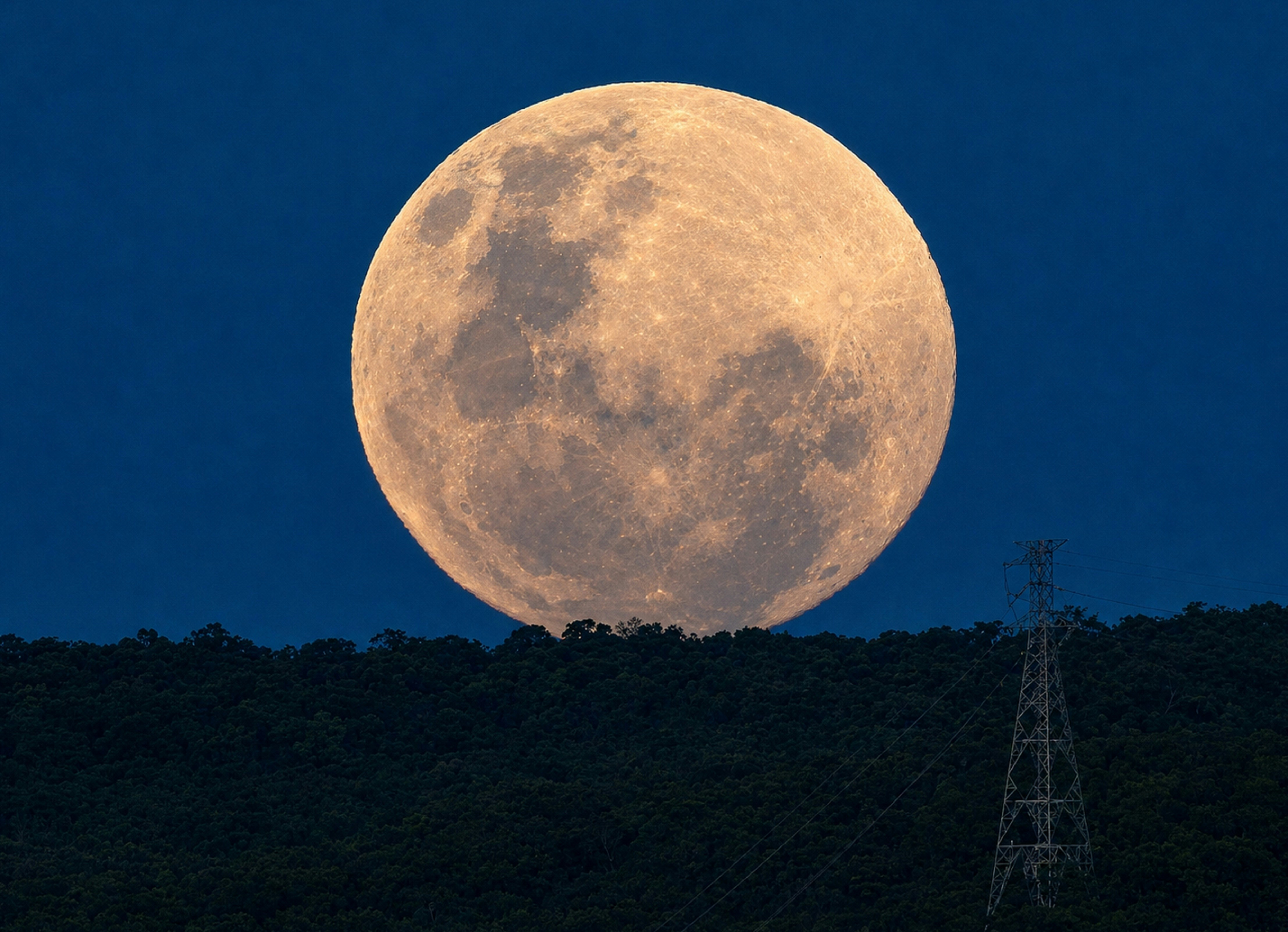 Full moon rising over a dark, tree-covered hill.