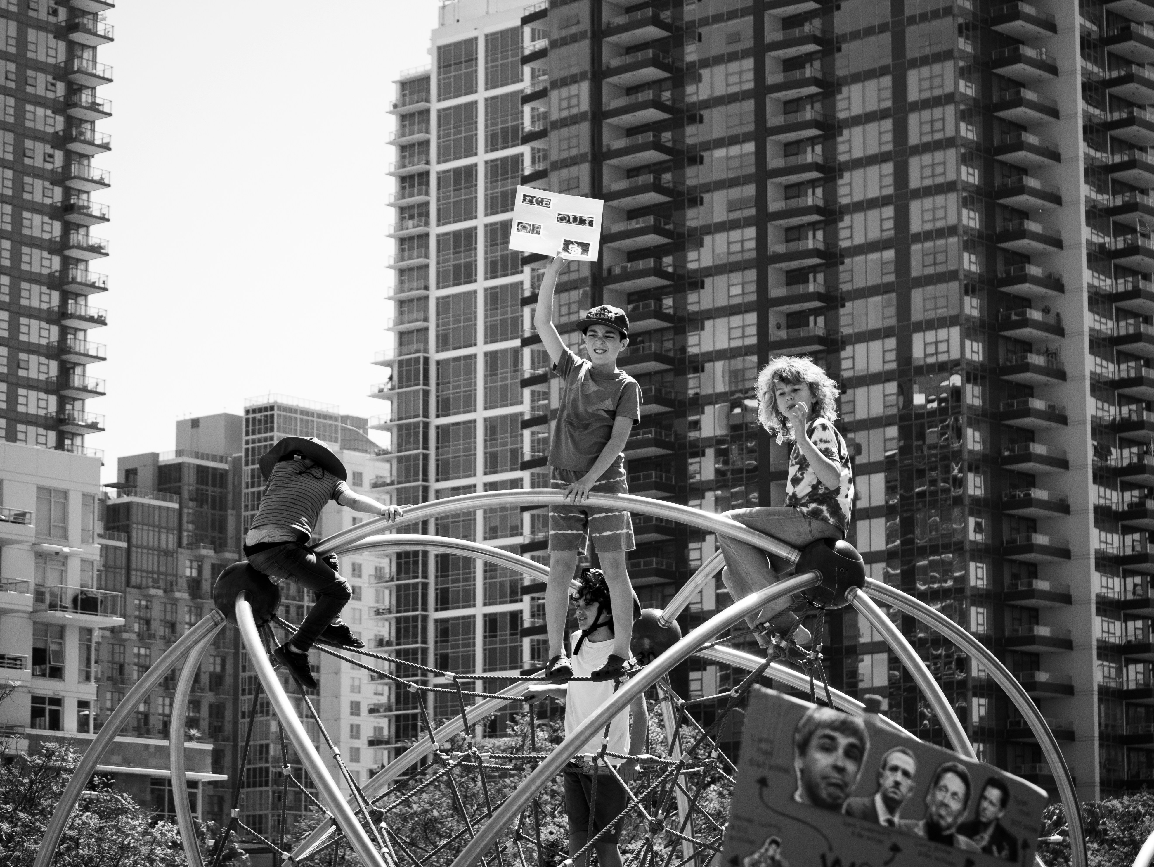 子どもたちが遊具に乗っていて、背後に市の建物が見えます