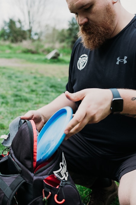 Person placing a disc golf disc into a bag at a wooded disc golf course