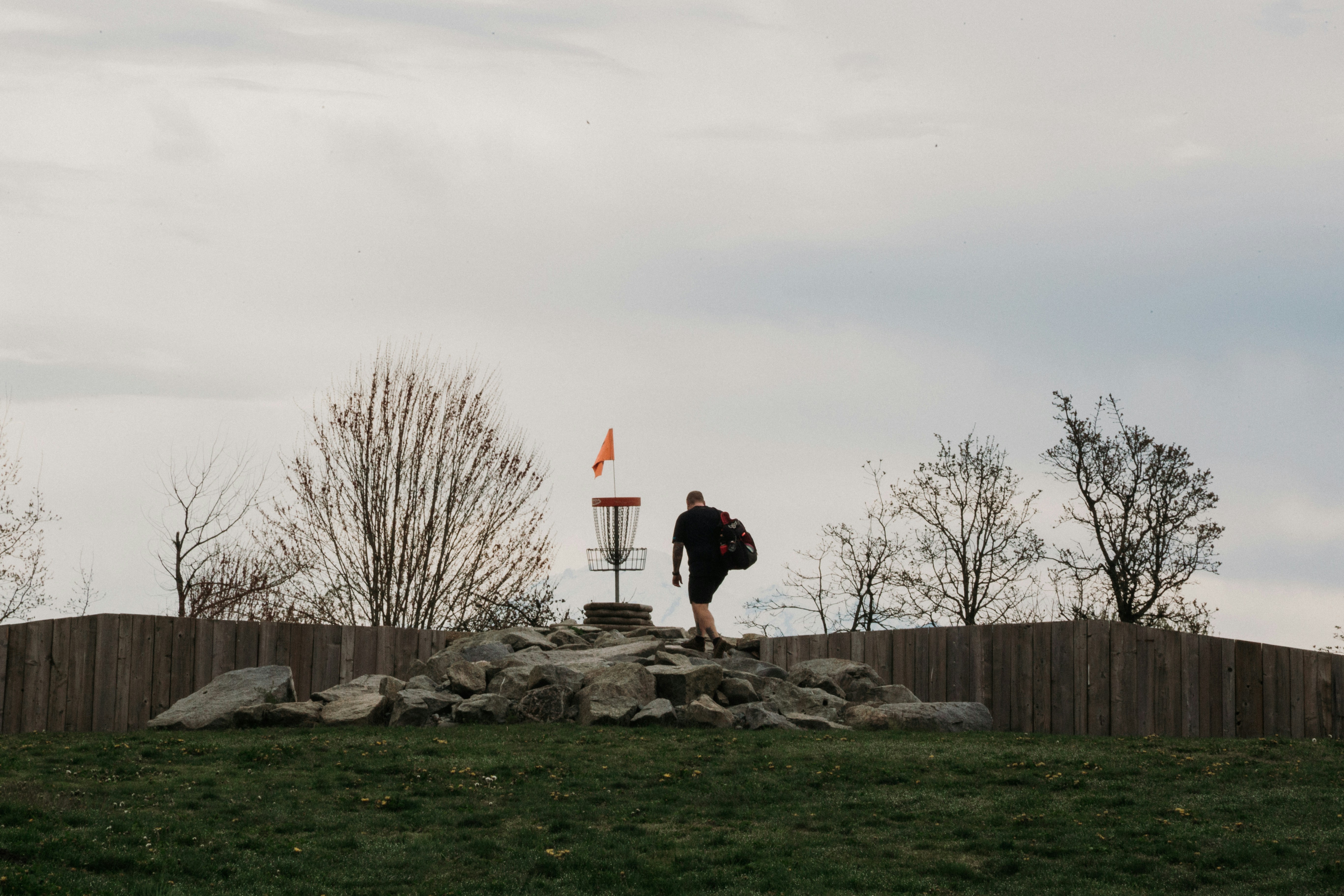 Man walking towards a disc golf basket on a hill.