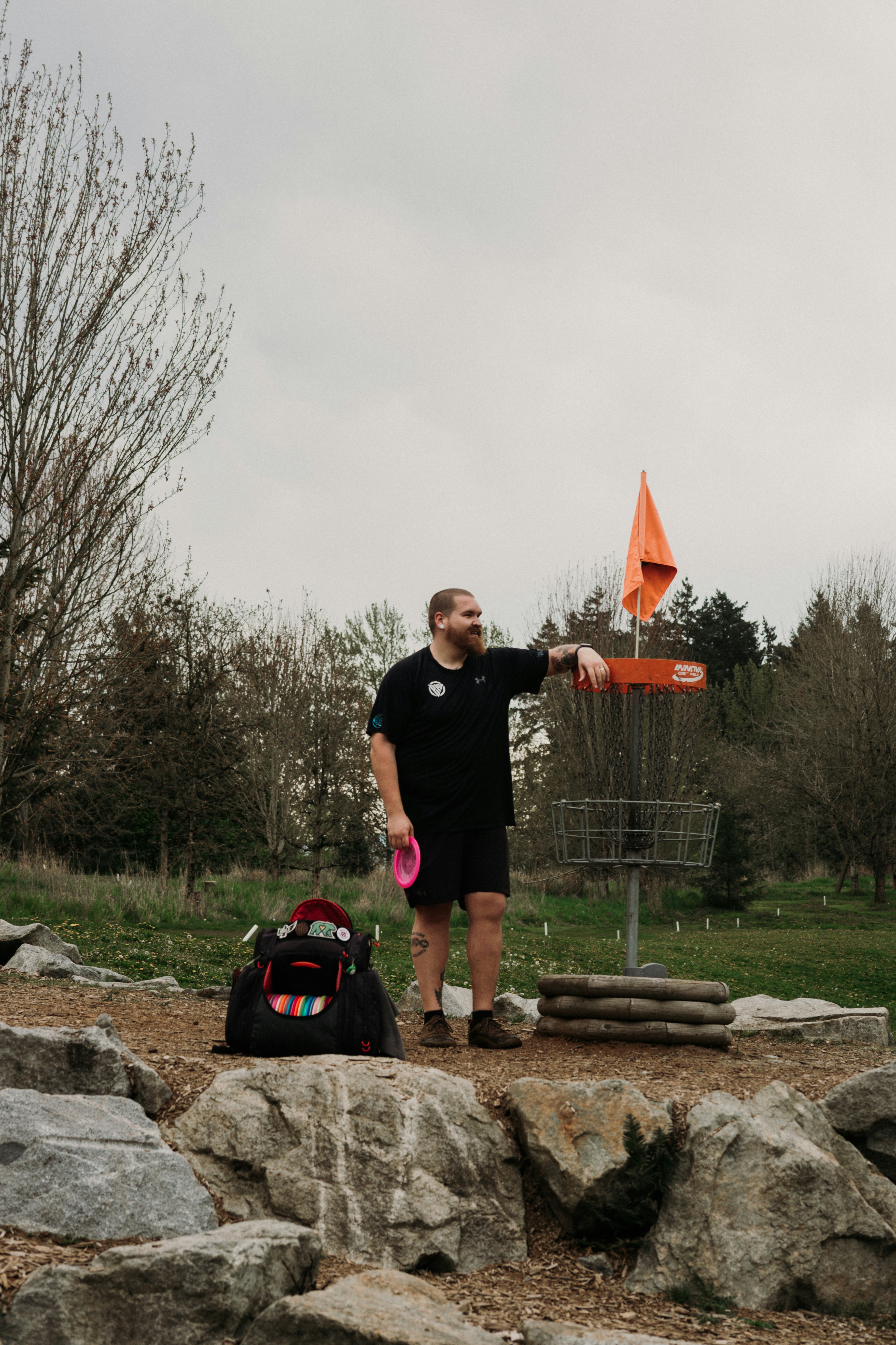 Man standing by disc golf basket with disc and bag