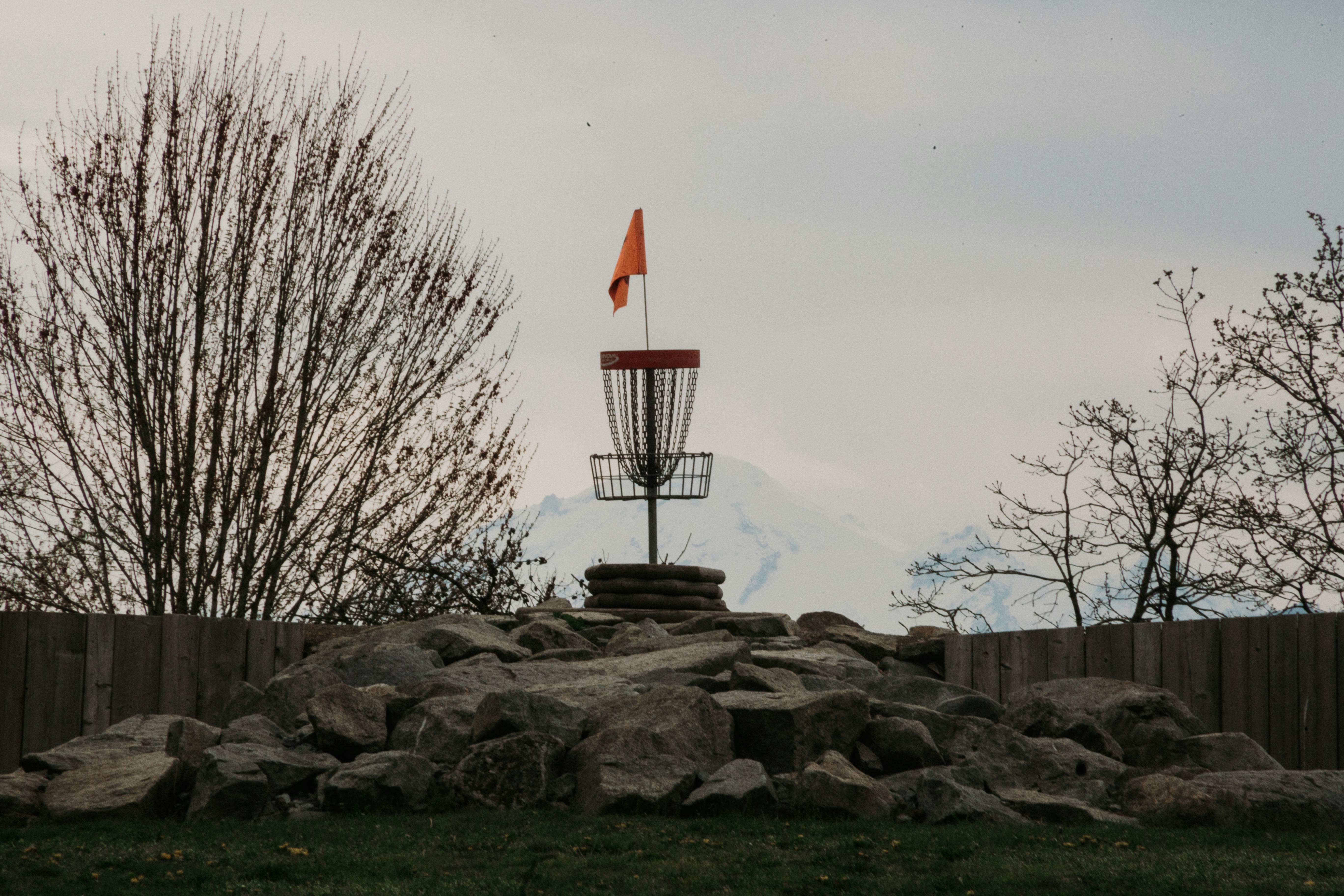 Disc golf basket with orange flag on rocky mound.