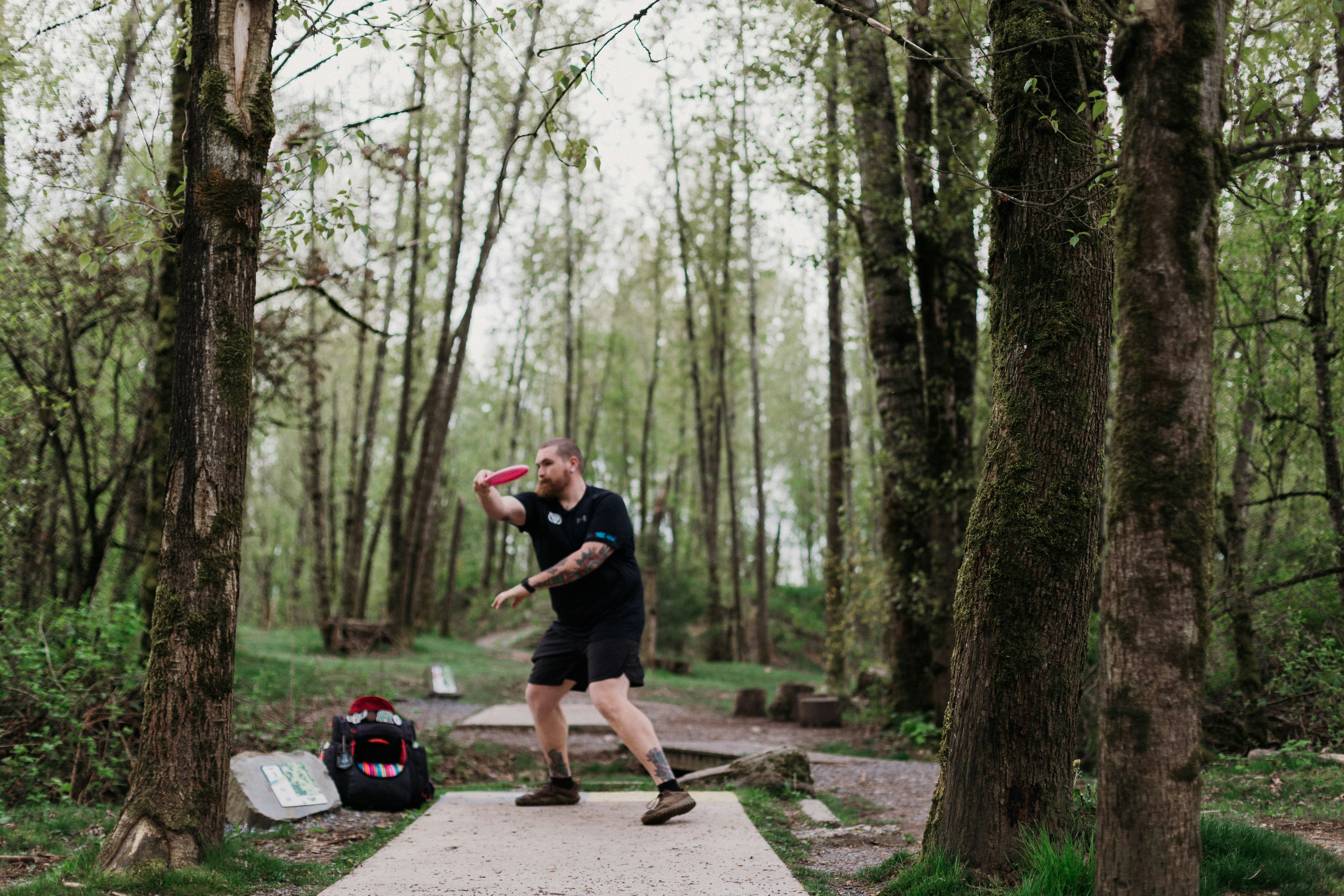Man throwing a disc golf disc in a wooded park