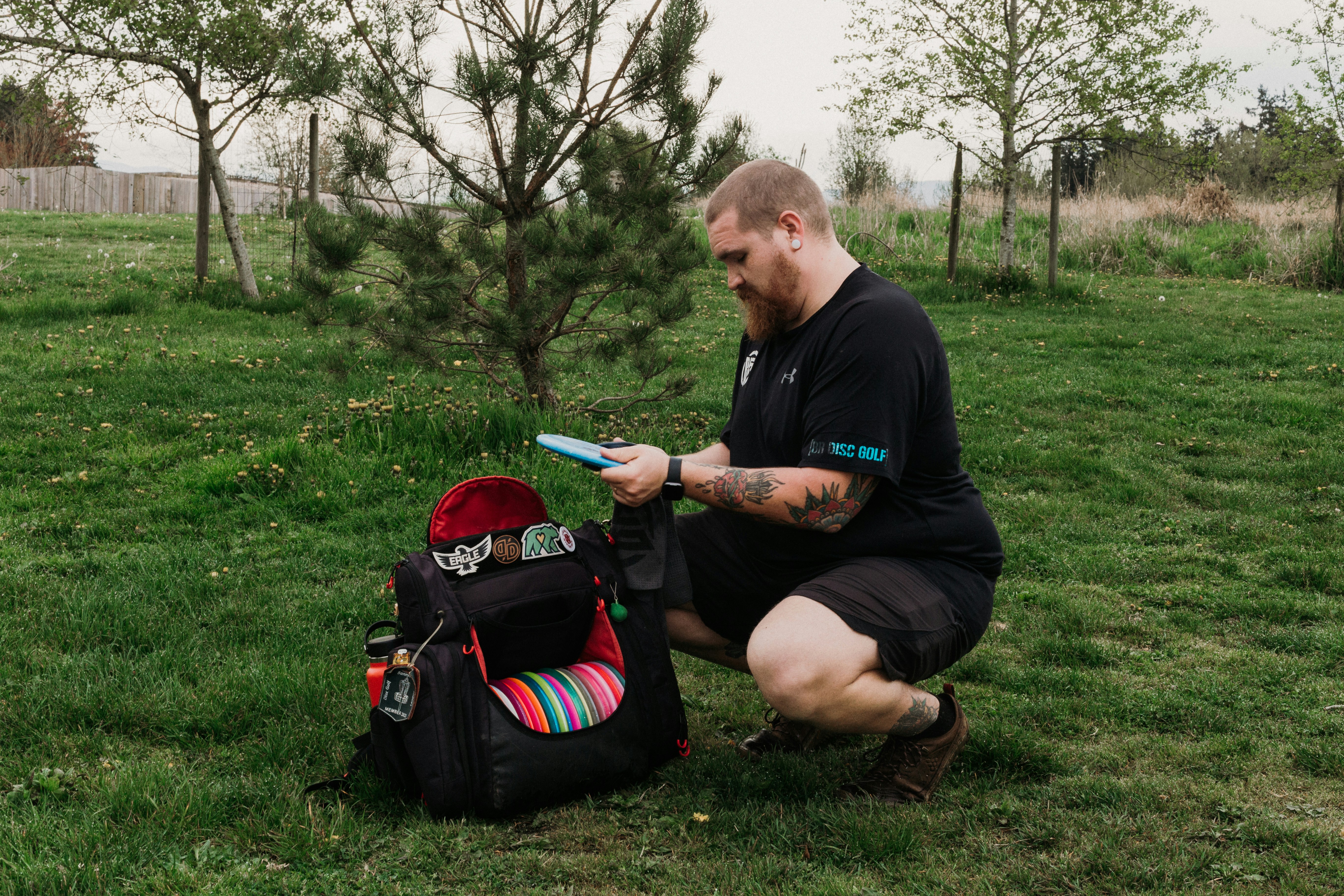 Man with disc golf bag in grassy field.