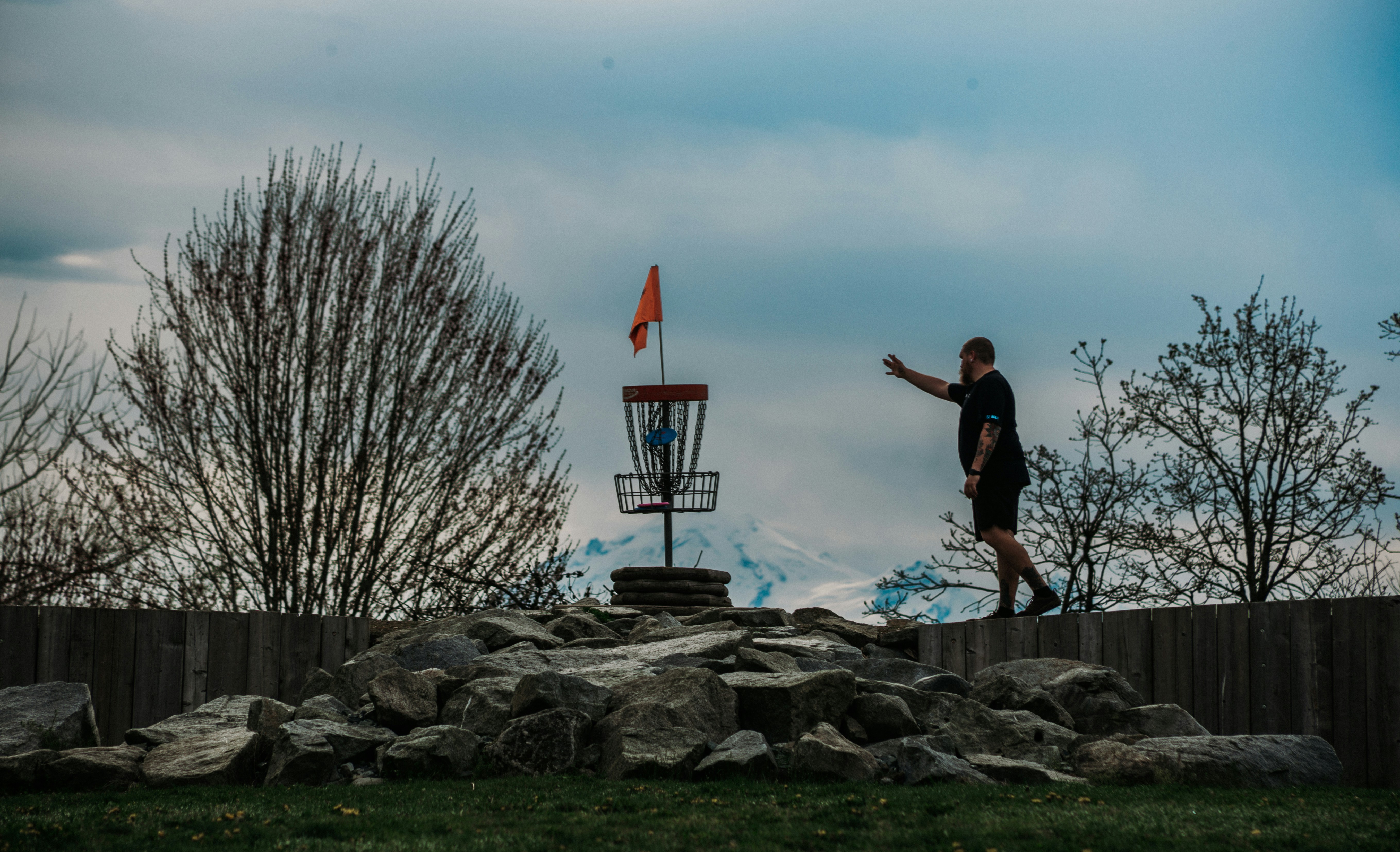 Man throwing disc golf disc towards basket on course
