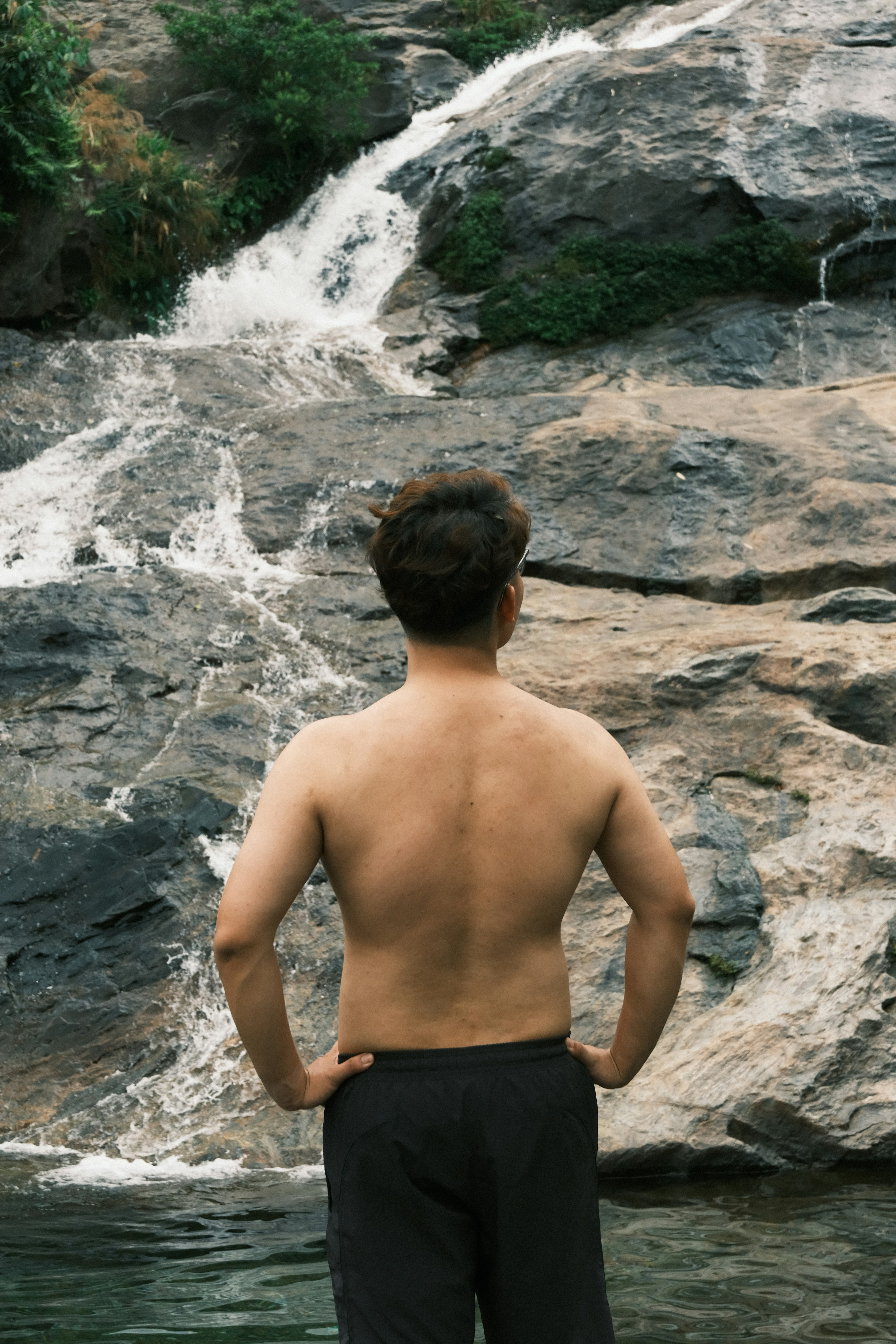 Homem parado ao lado de uma cachoeira rochosa