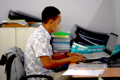 Man wearing mask working on laptop at desk
