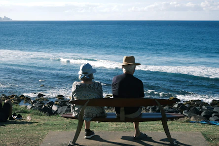 Elderly couple sits on bench overlooking ocean waves