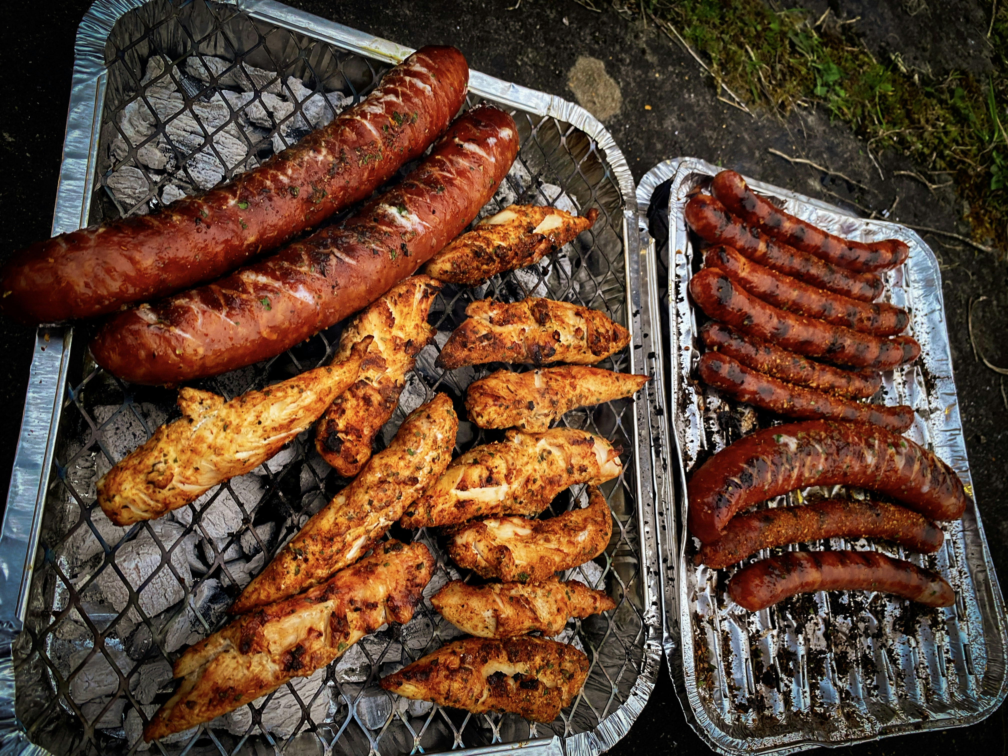 Sausages and chicken pieces grilling on a barbecue.