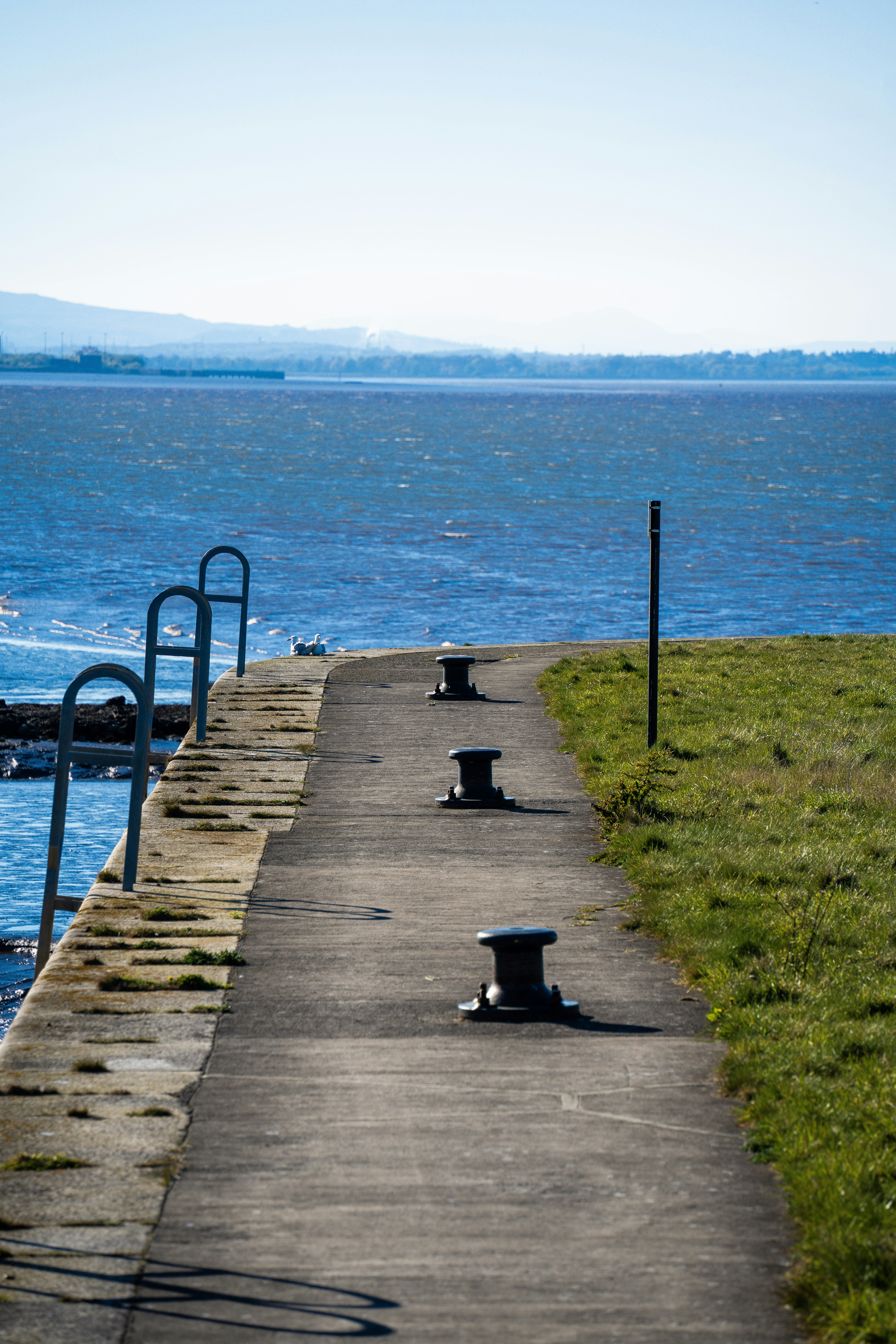 A concrete walkway beside the ocean with bollards.