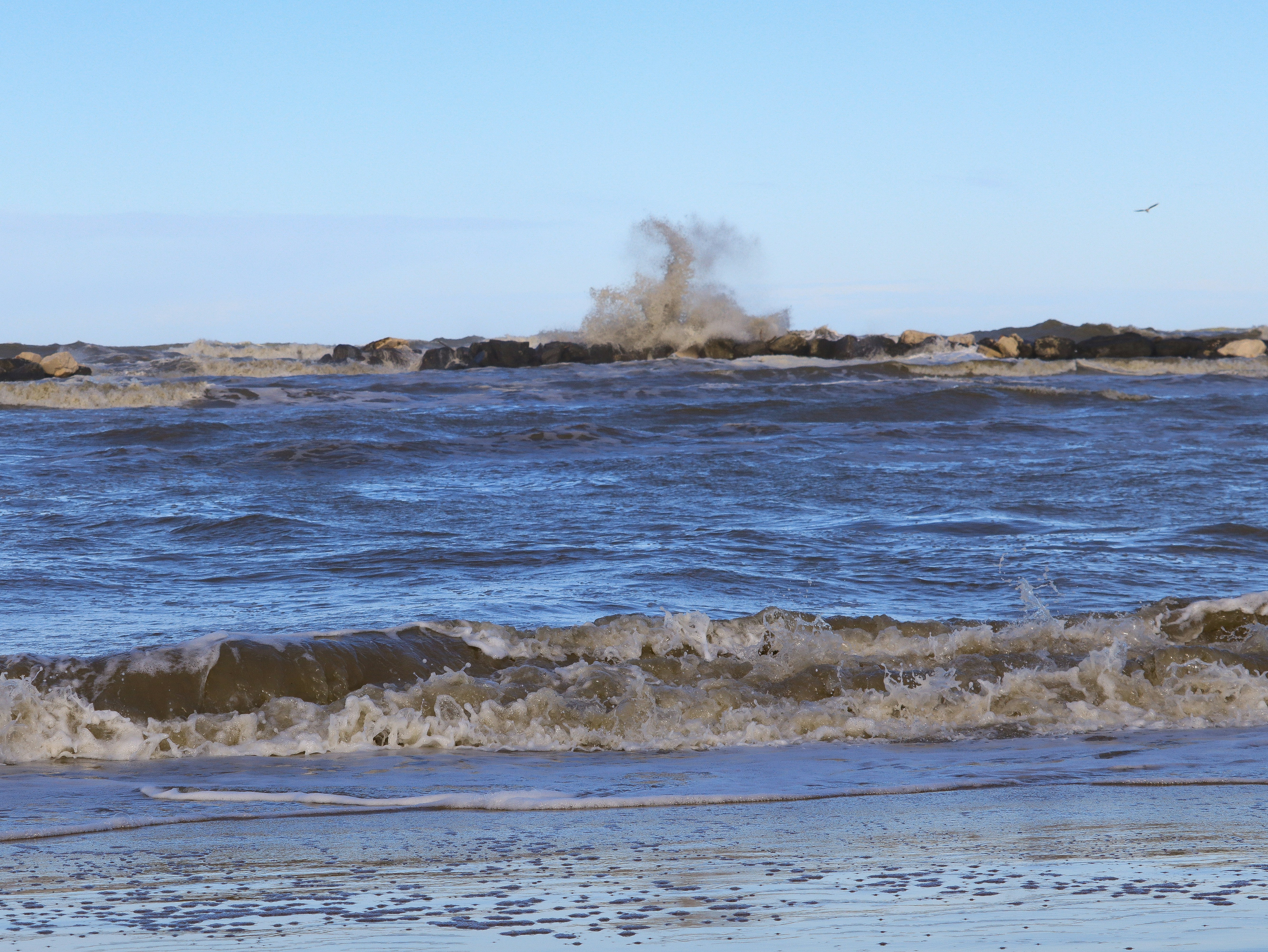 Waves crashing against rocks under a clear blue sky
