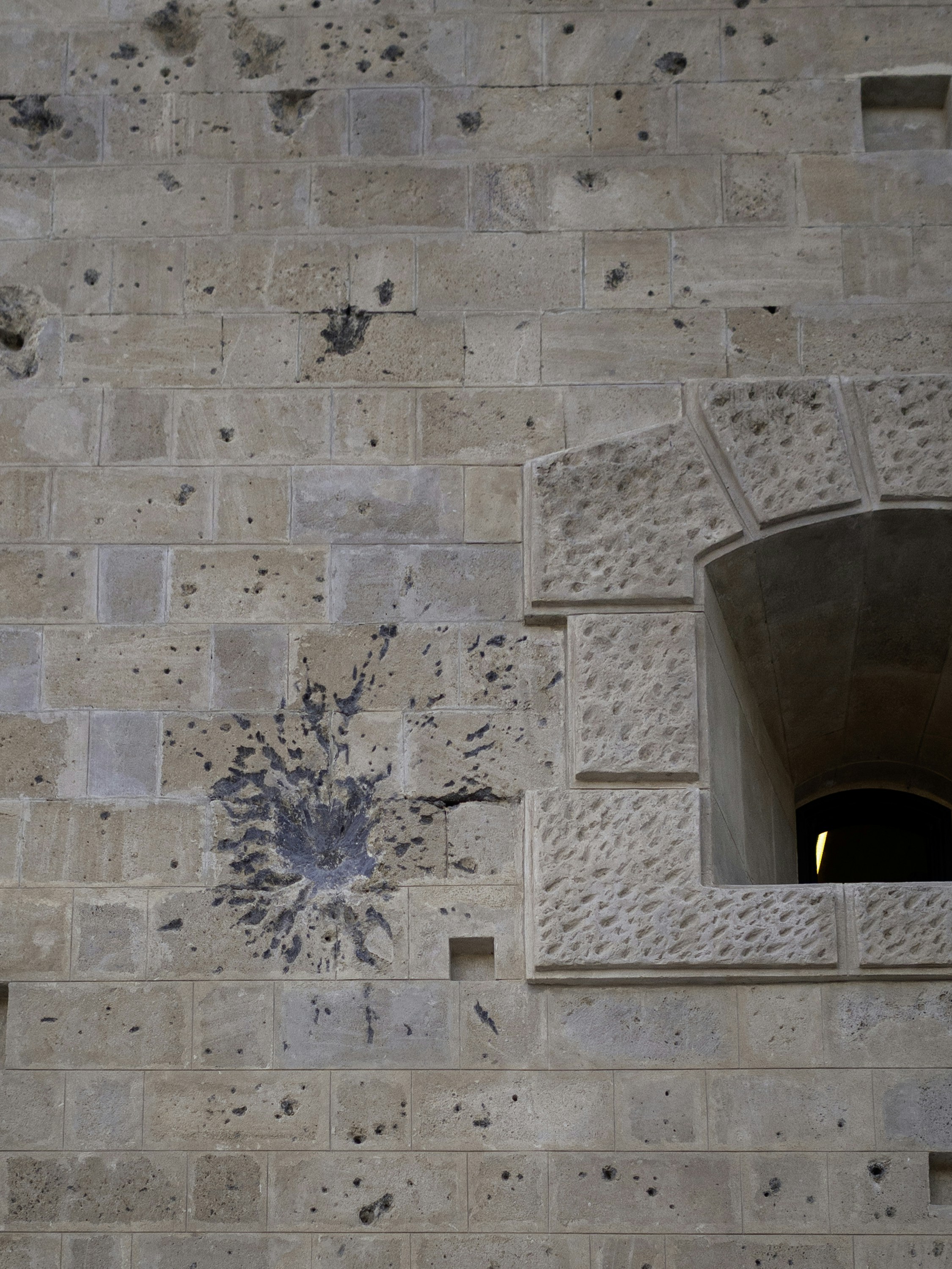 Stone wall with a large impact mark and window.