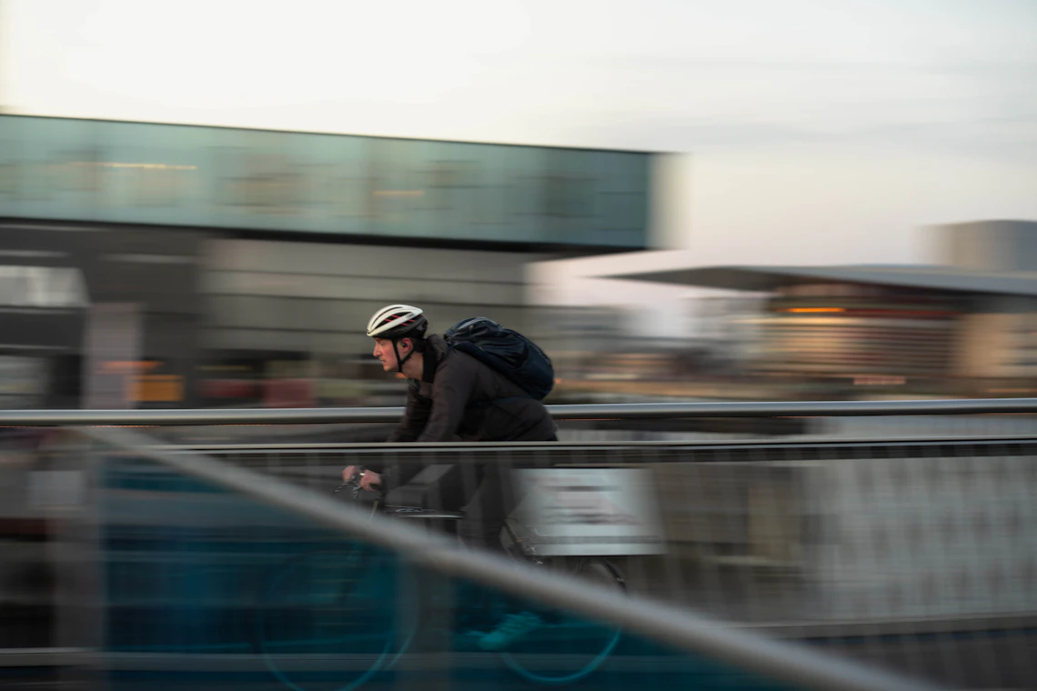 Cyclist with a backpack riding across a modern city bridge
