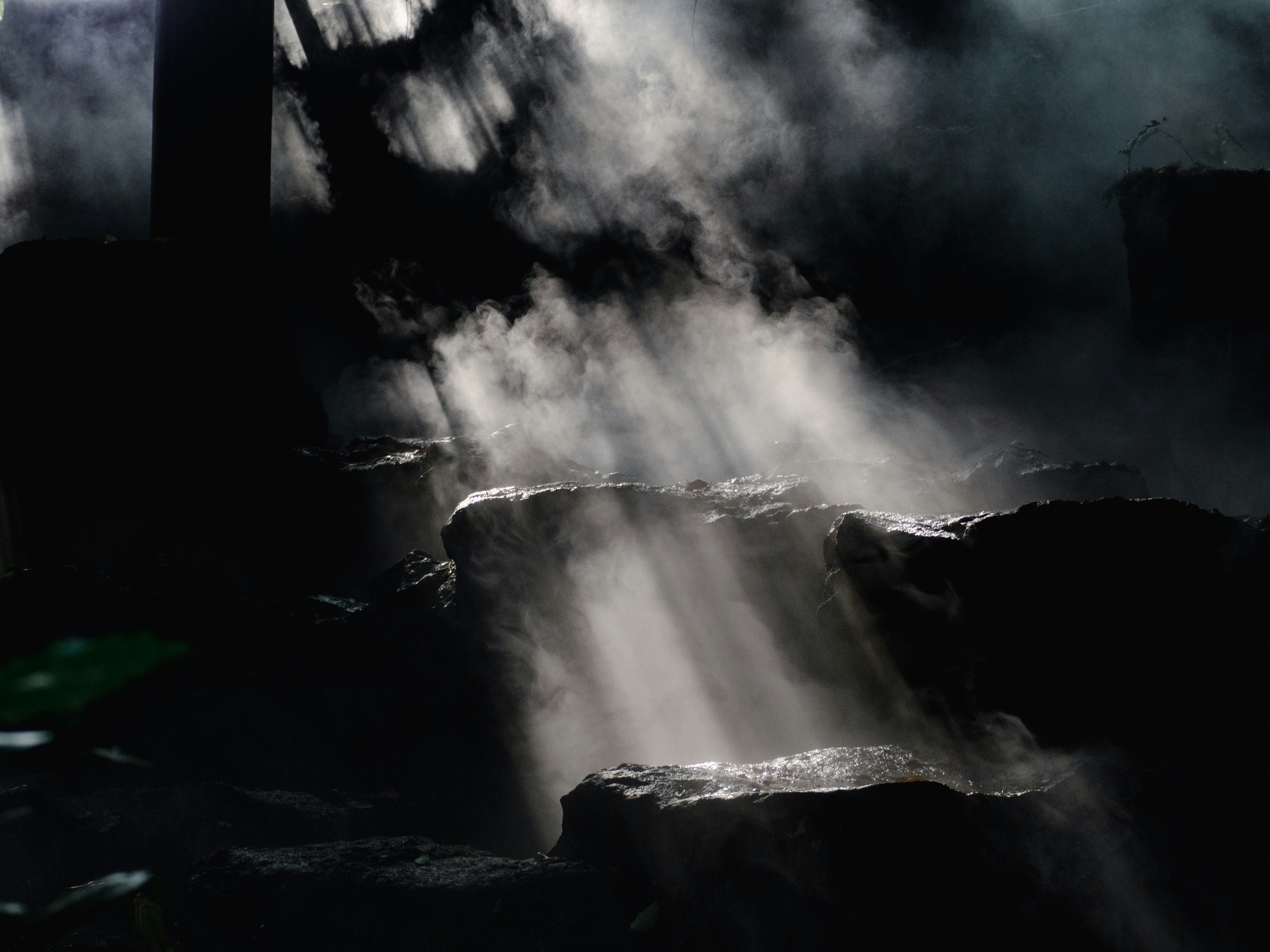 Sunlight streams through mist onto dark rocks.