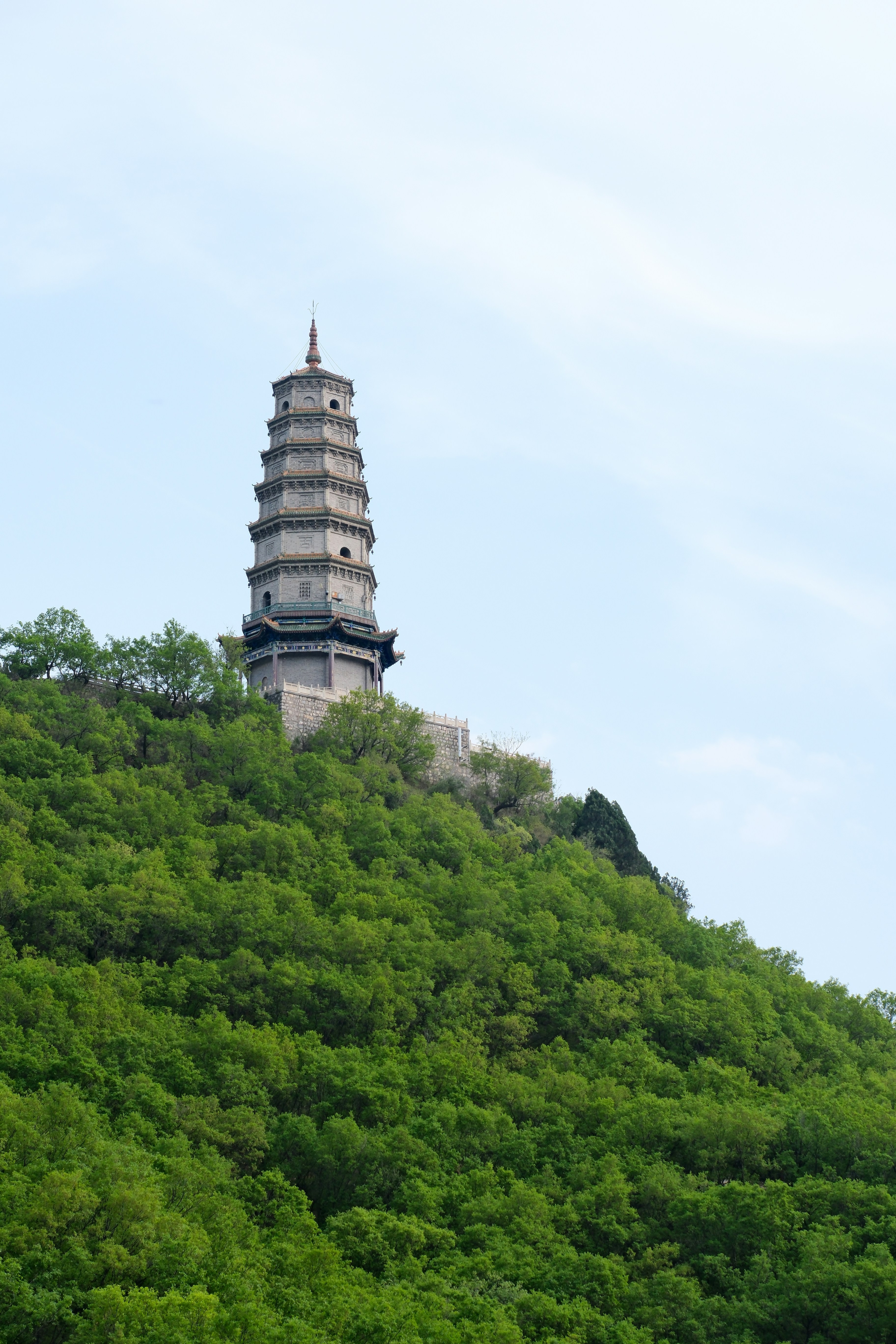 A tall pagoda stands atop a lush green hill.
