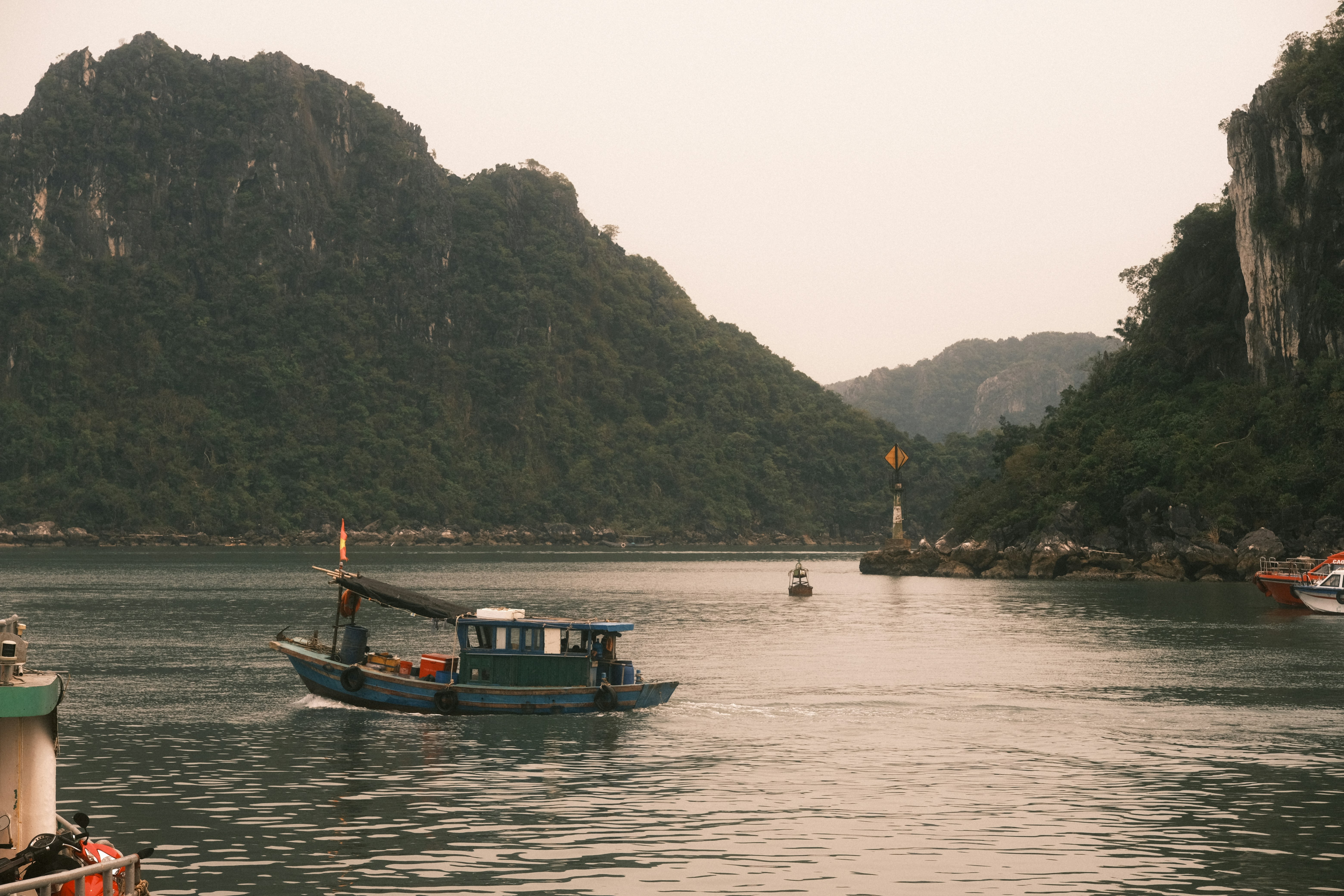 A small boat sails on the water between green mountains.