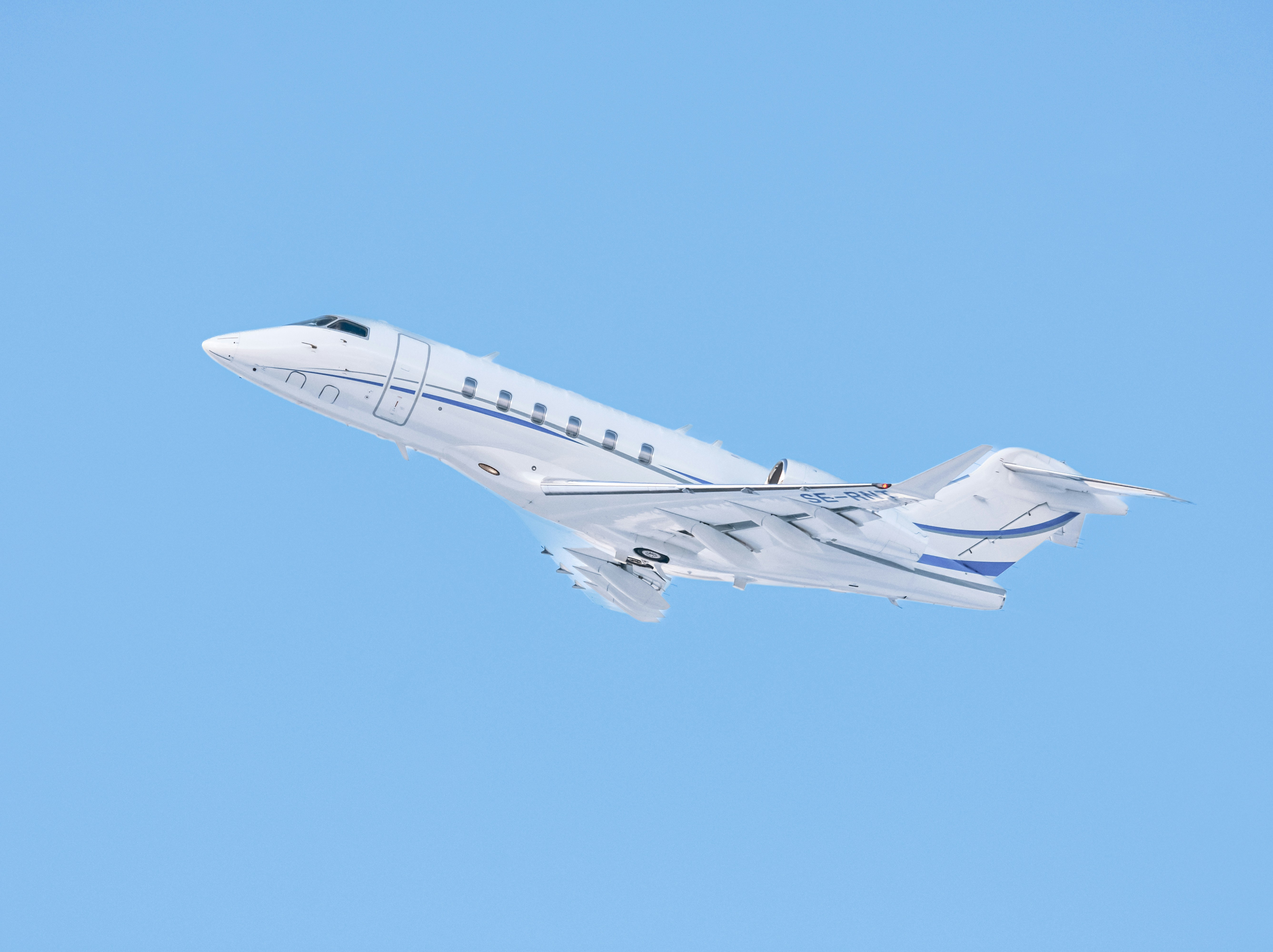 A white private jet ascends into a clear blue sky.