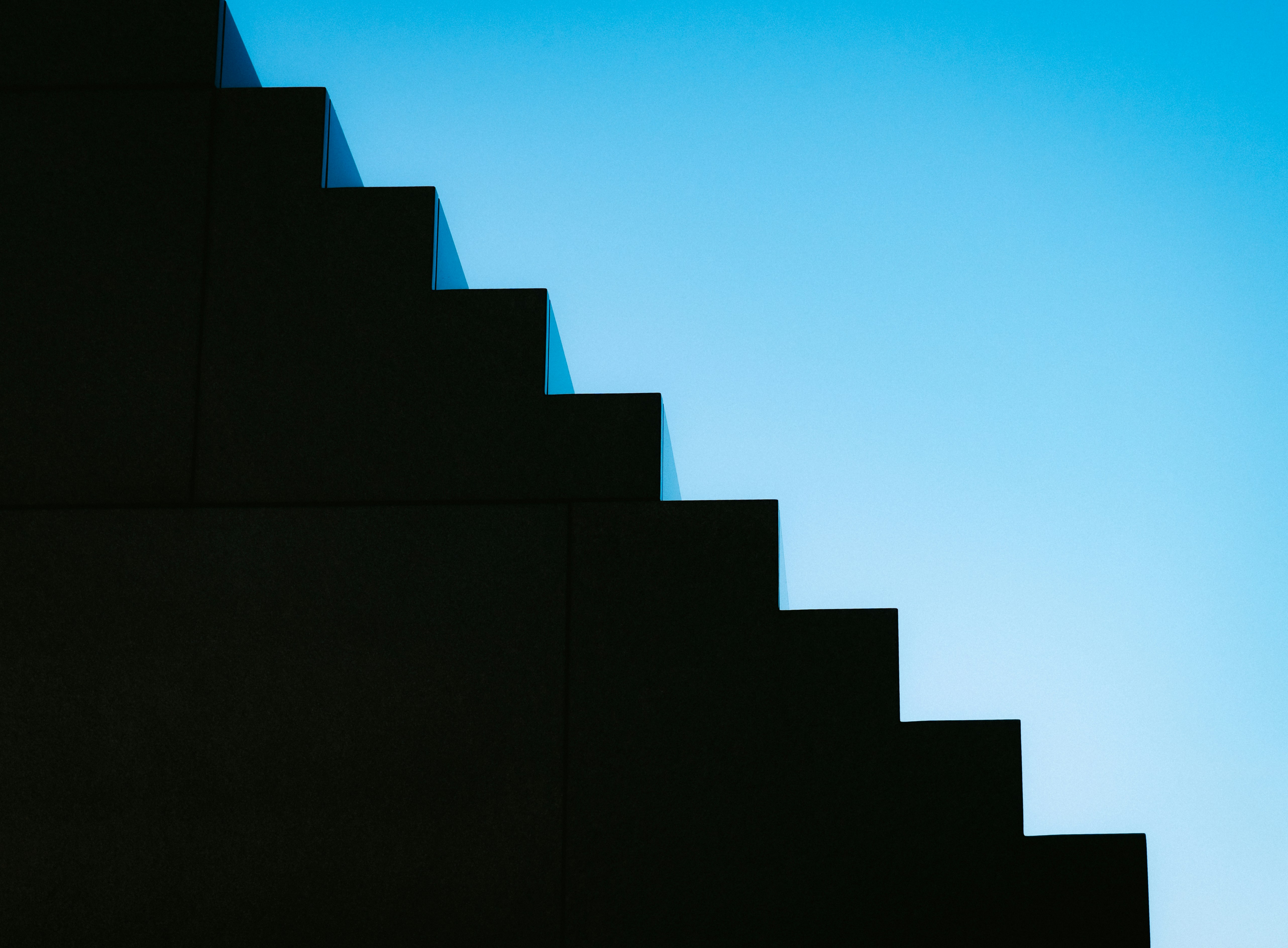 Escadas escuras sobem contra um céu azul claro.