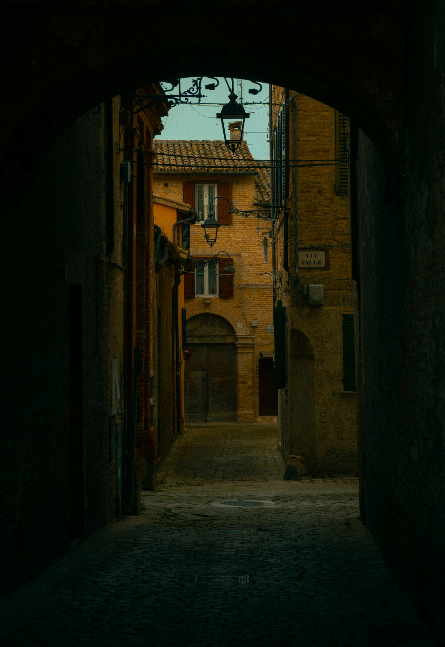 A dark stone archway opening onto a sunlit ochre street