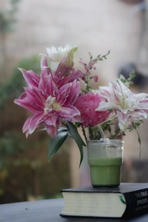 Pink lilies and a green drink on a book.
