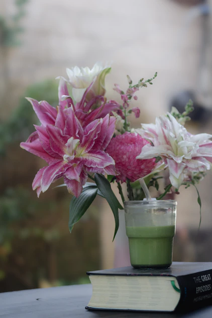 Pink lilies and a green drink on a book.
