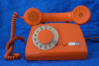 An orange rotary dial telephone on a blue background