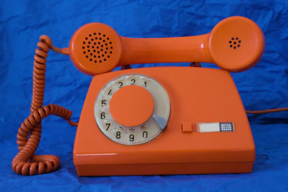 An orange rotary dial telephone on a blue background