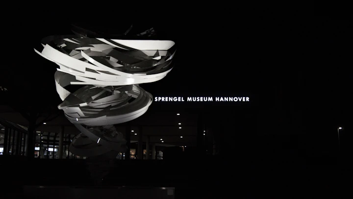 Abstract sculpture outside the Sprengel Museum Hannover at night — a quiet metallic mass under low light, kin to Pavel Ostrowski's Quiet machinery