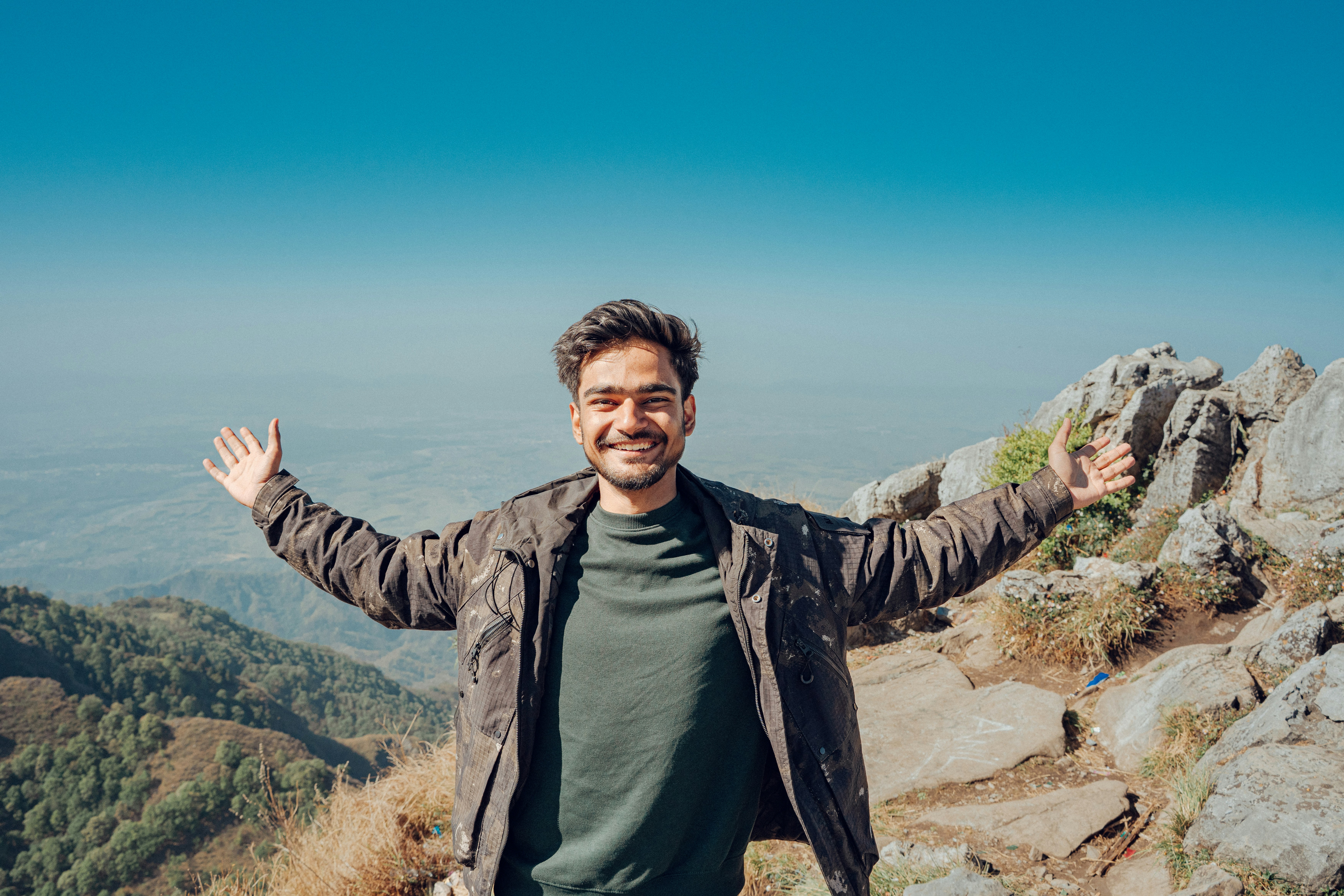 Um homem sorridente com os braços estendidos em uma montanha.