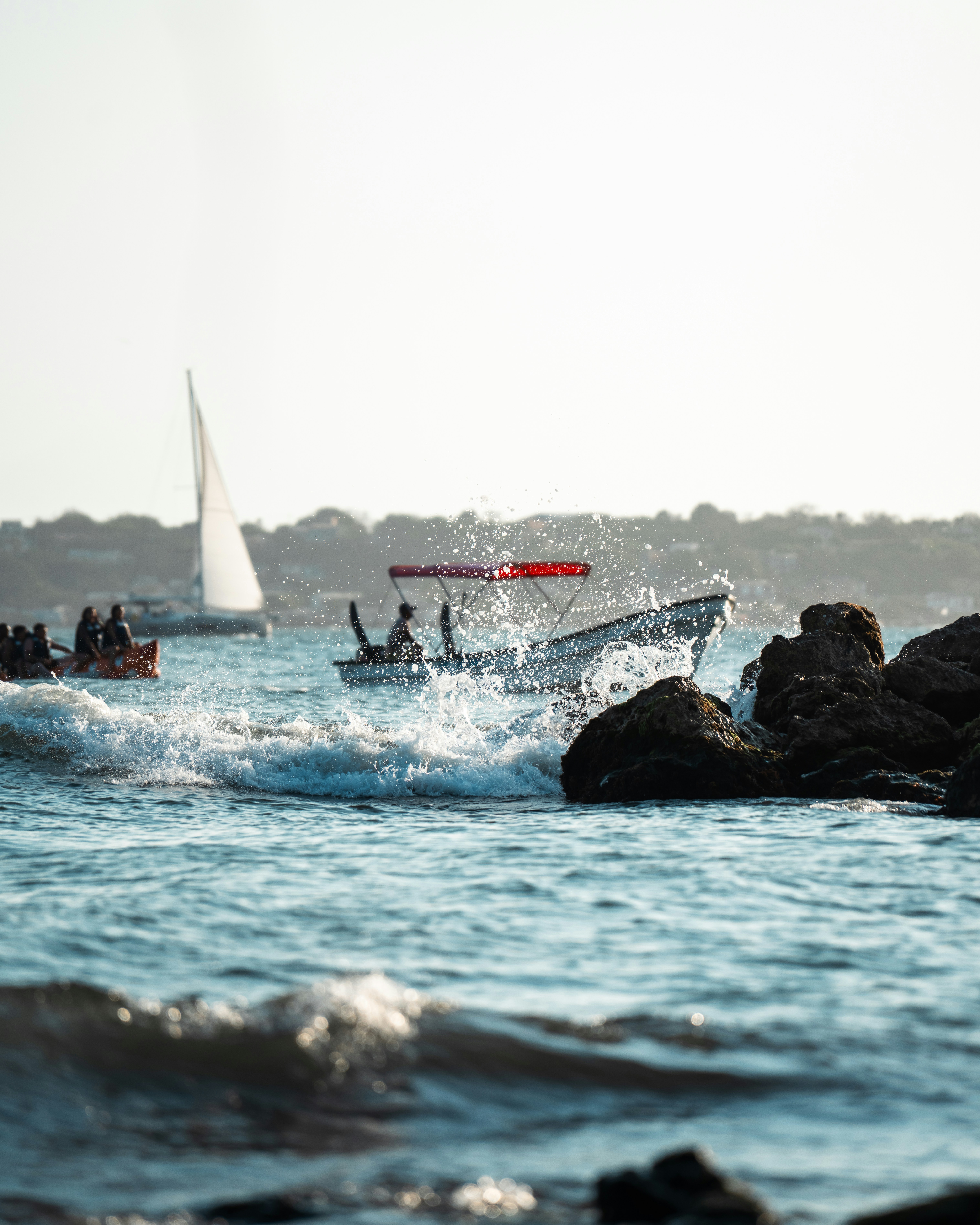 Boats navigating choppy ocean waters near rocky shore.