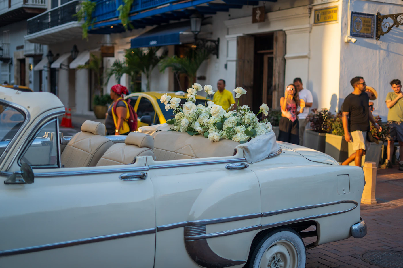A vintage white convertible wedding car decorated with white roses and ribbons parked on a cobblestone street in Cartagena Colombia Old City