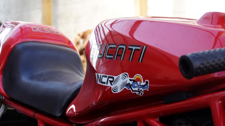 Close-up of a red Ducati fuel tank with the maker's logo, evoking the round-case 750 GT