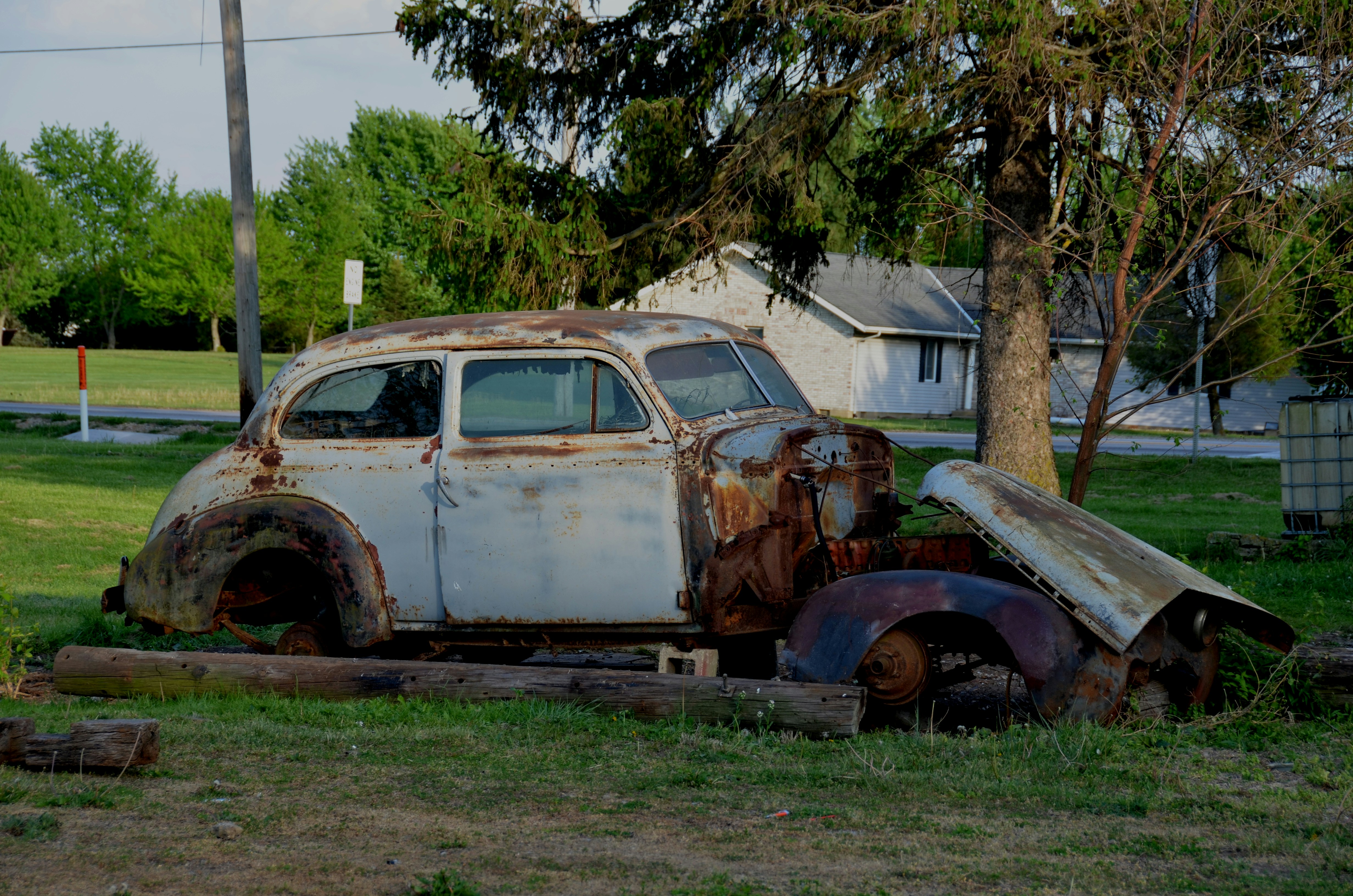 Une vieille voiture rouillée est abandonnée dans un champ herbeux.