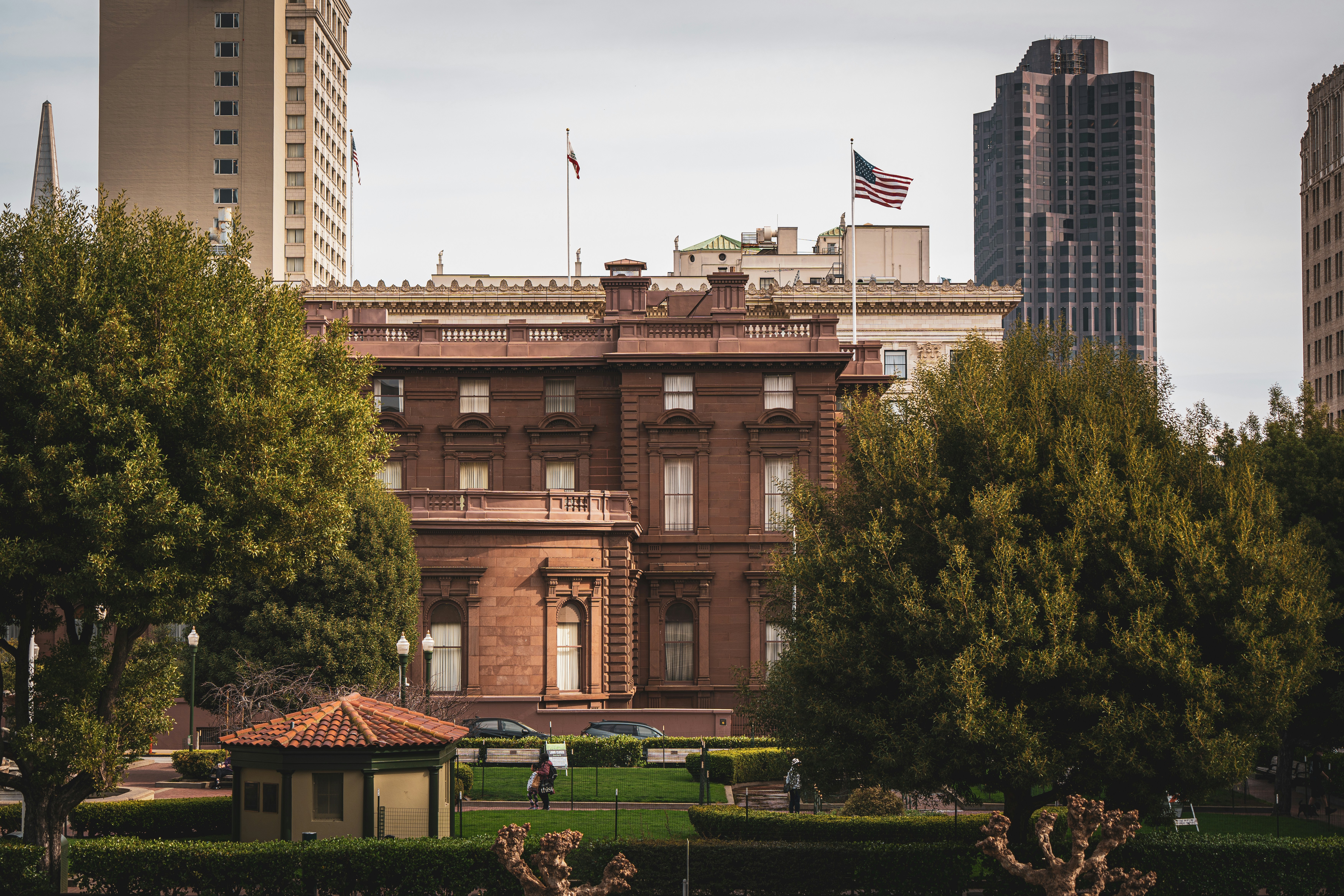 Historic mansion surrounded by trees and city buildings.