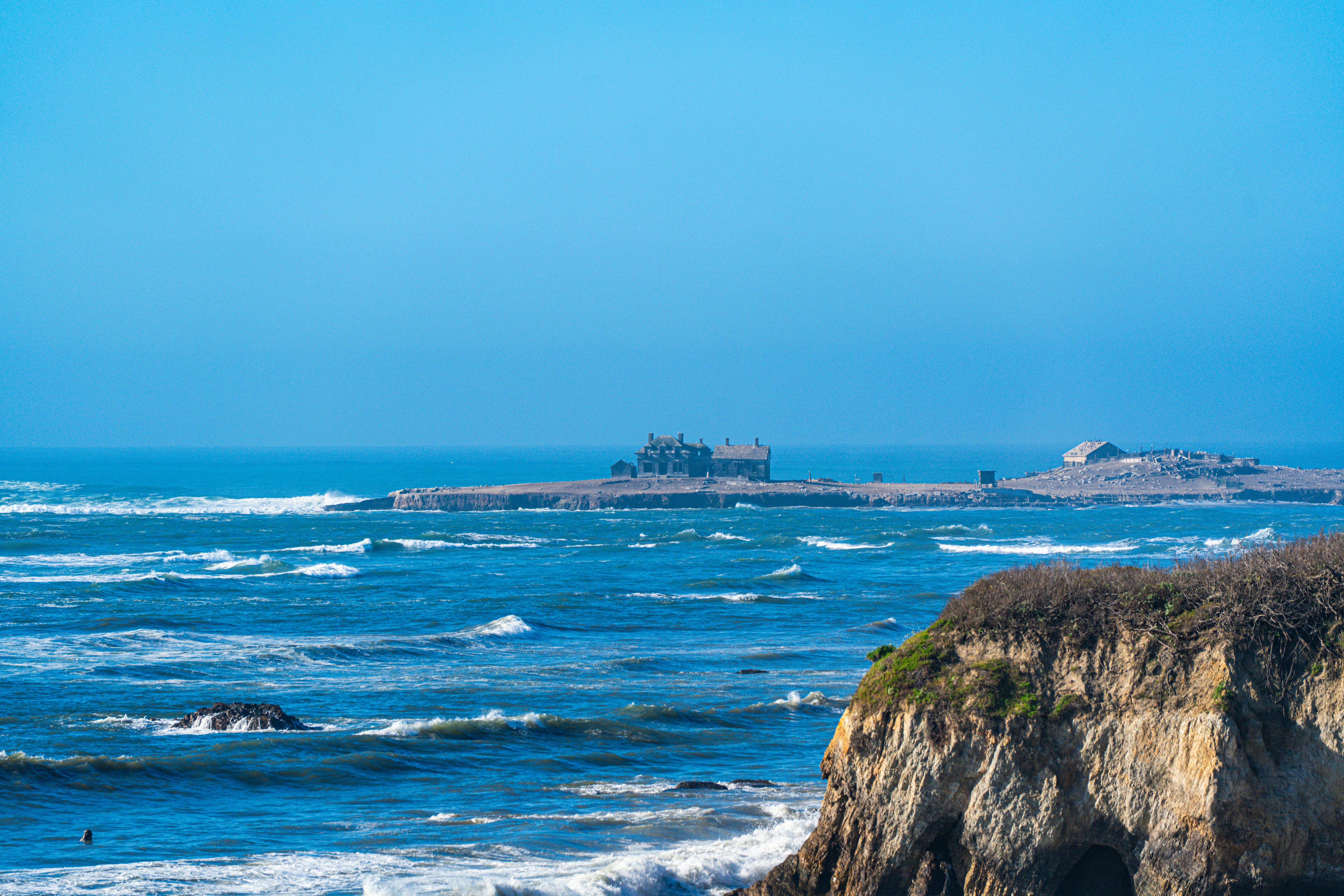 Waves crash on a rocky coastline with a distant island.