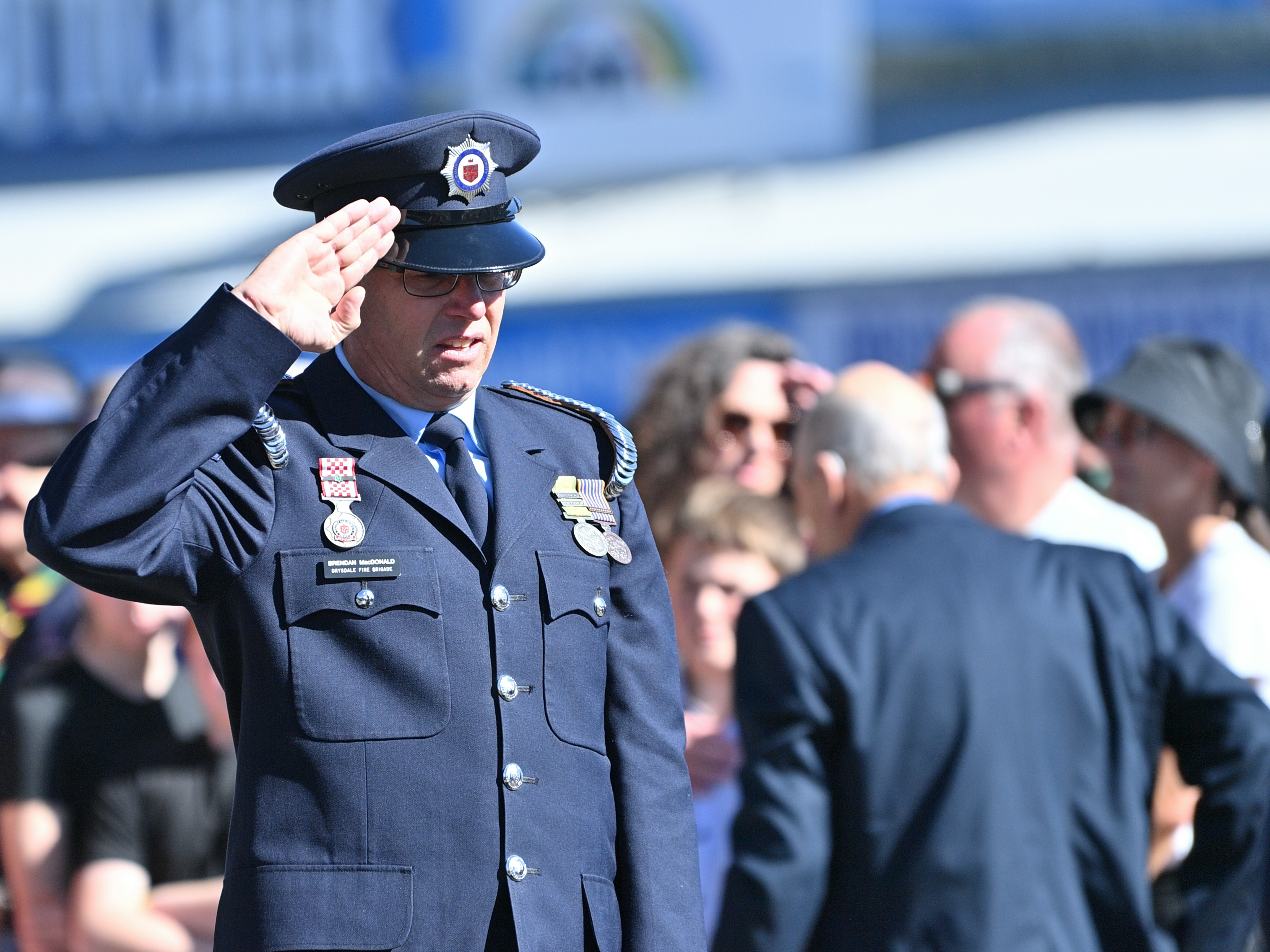 Man in uniform salutes during an outdoor ceremony.
