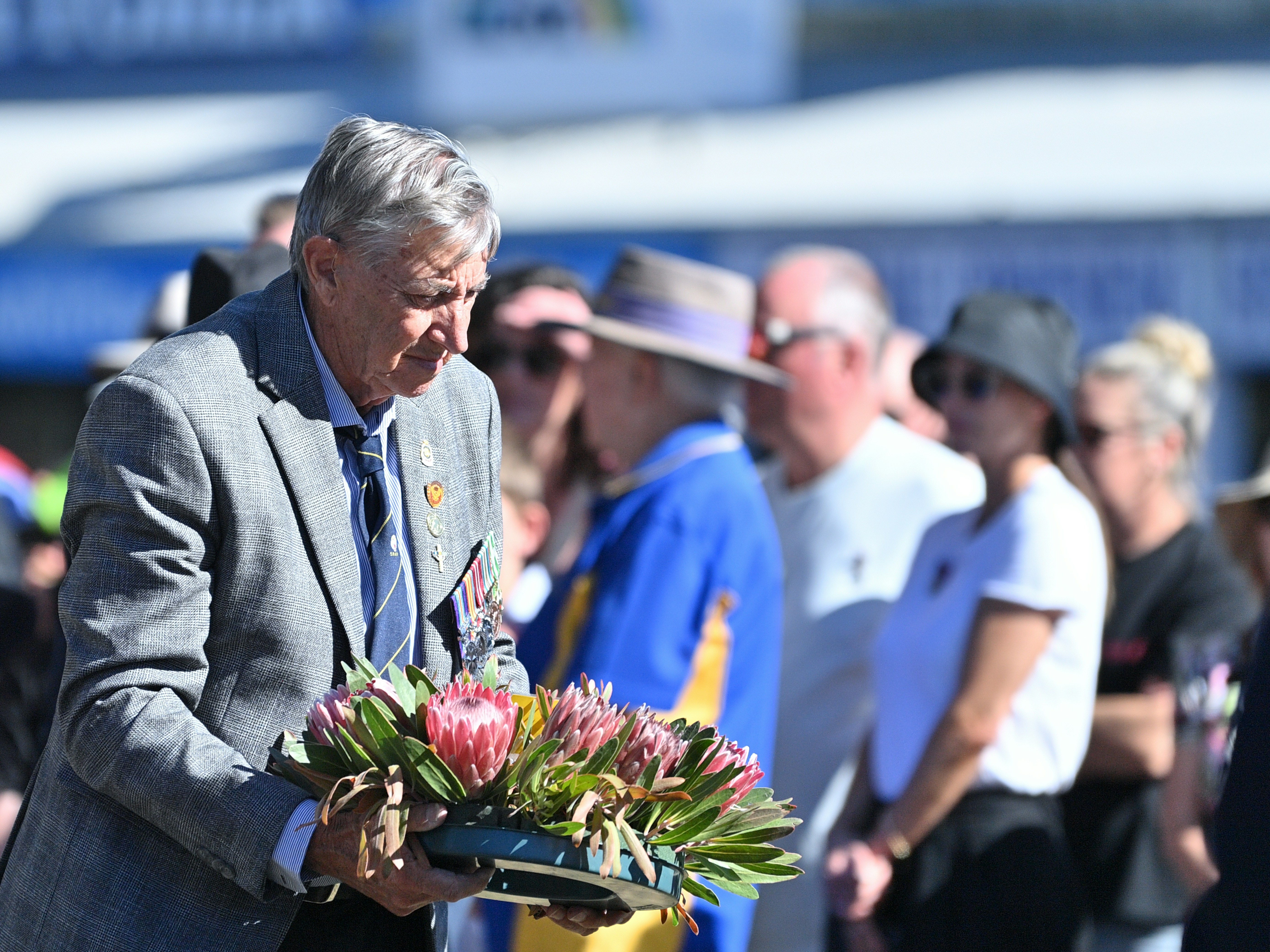 Man in suit lays wreath with flowers at outdoor event