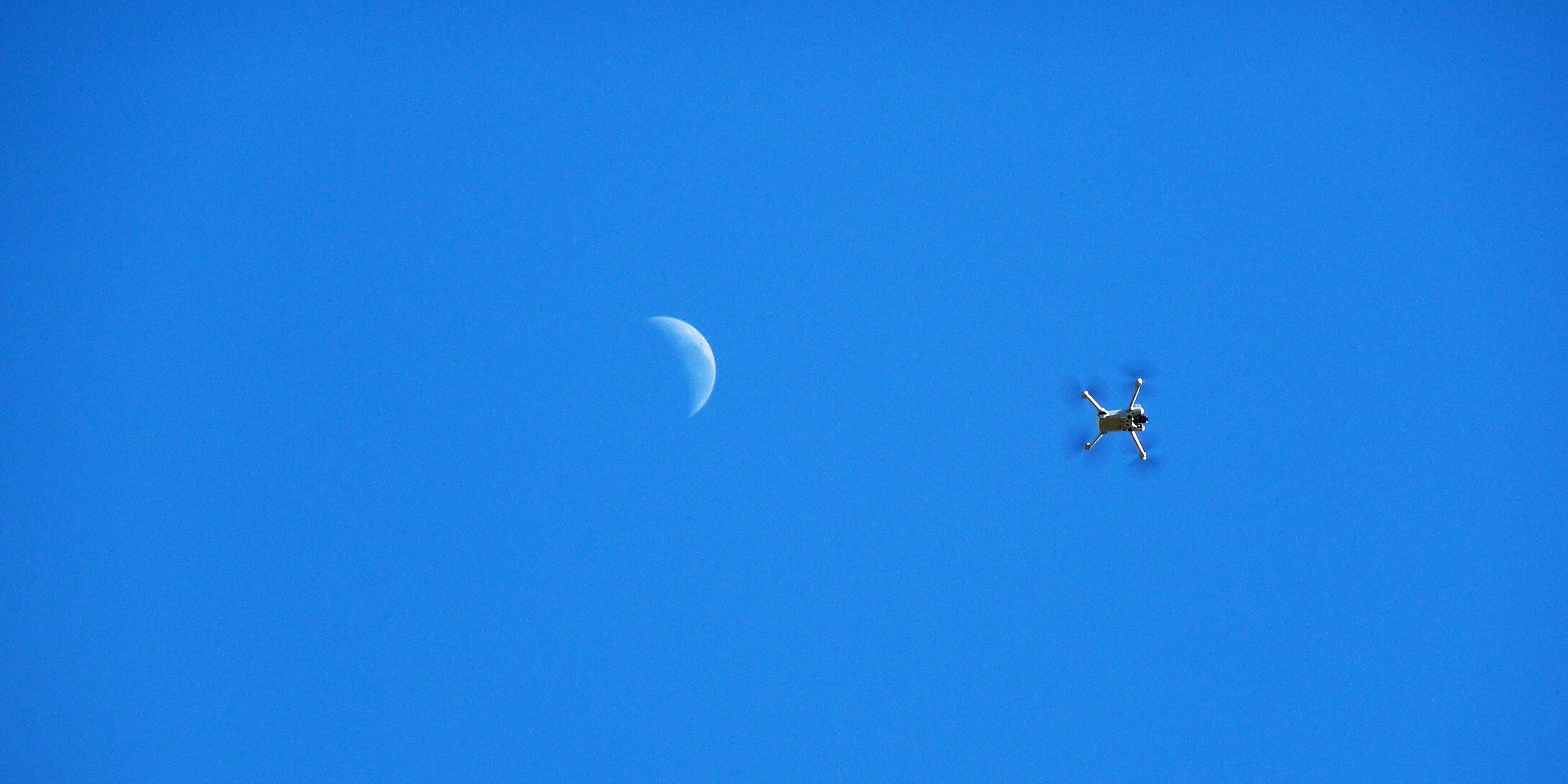 Um drone voa perto de uma lua crescente no céu.
