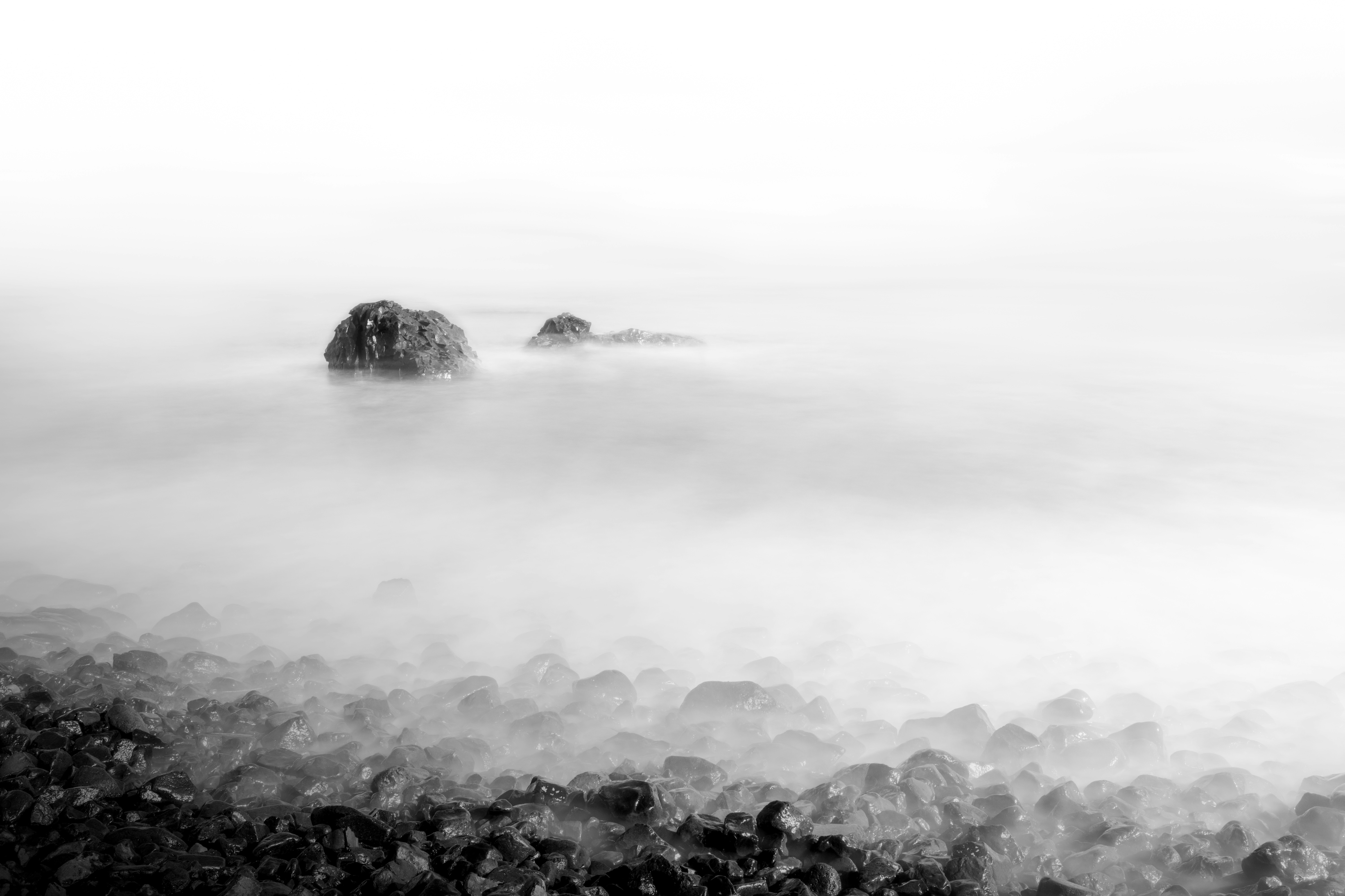 Misty ocean rocks with blurred water and shoreline.