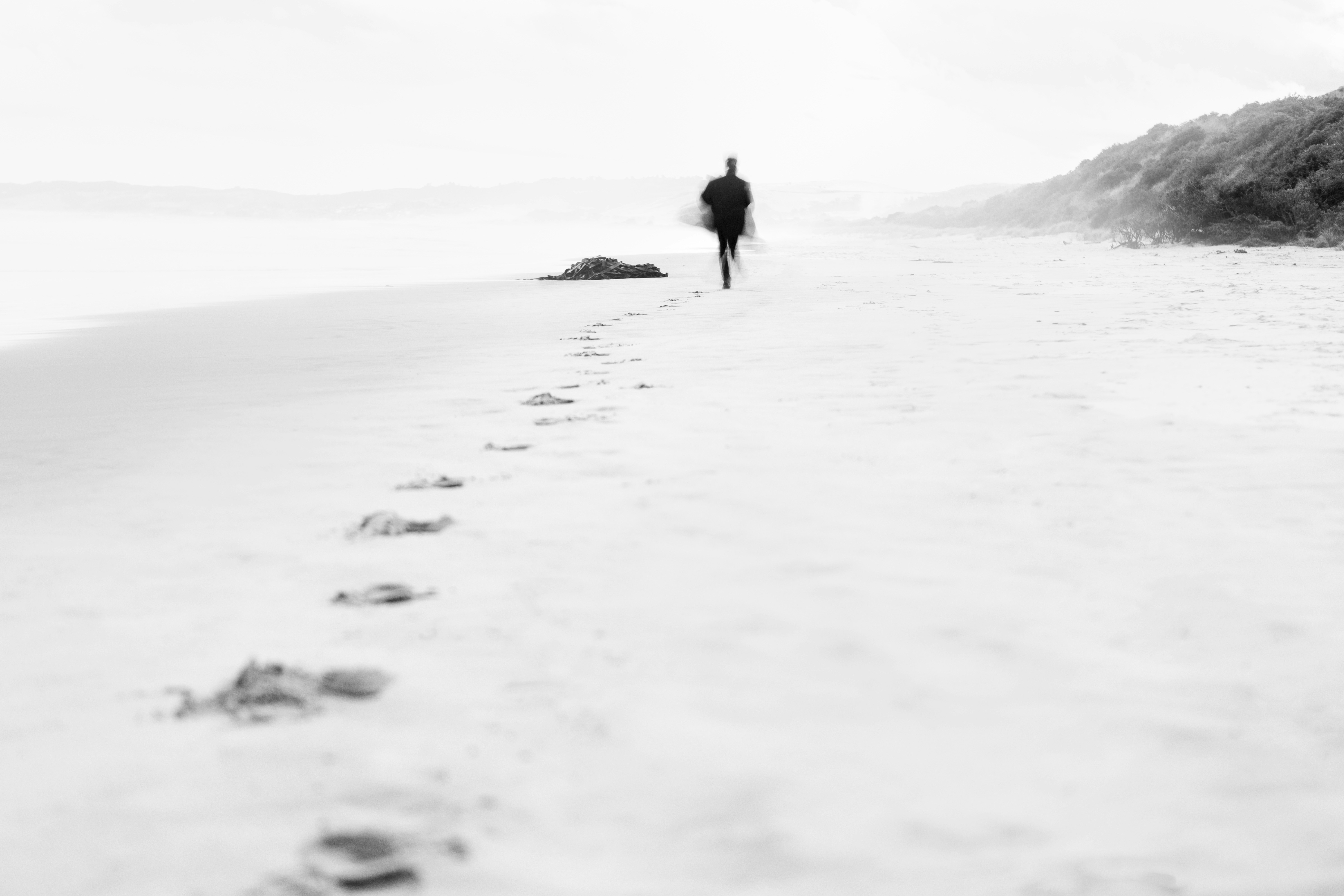 A lone figure walks on a sandy beach leaving footprints.