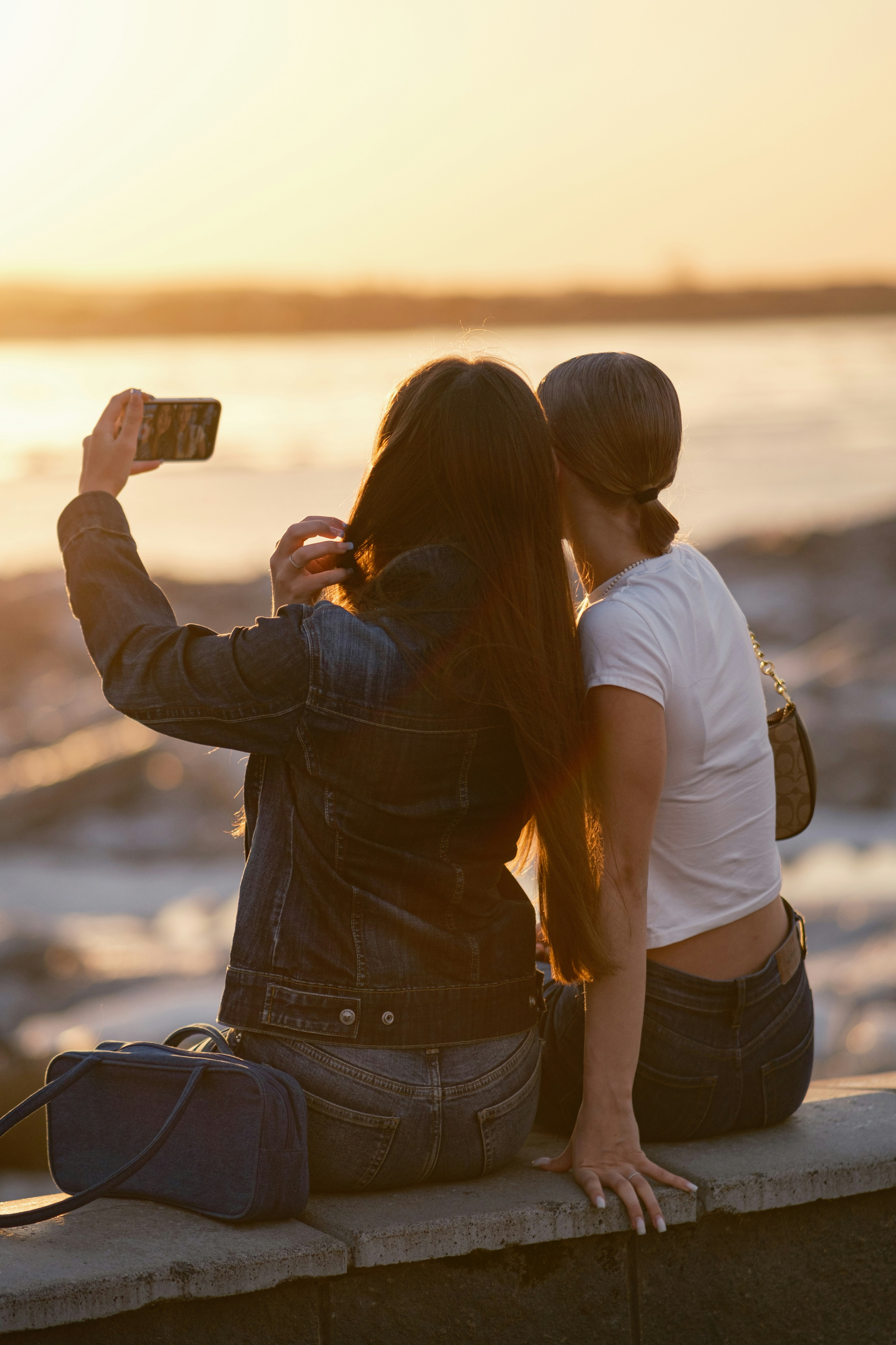 Two women taking a selfie by the water at sunset.