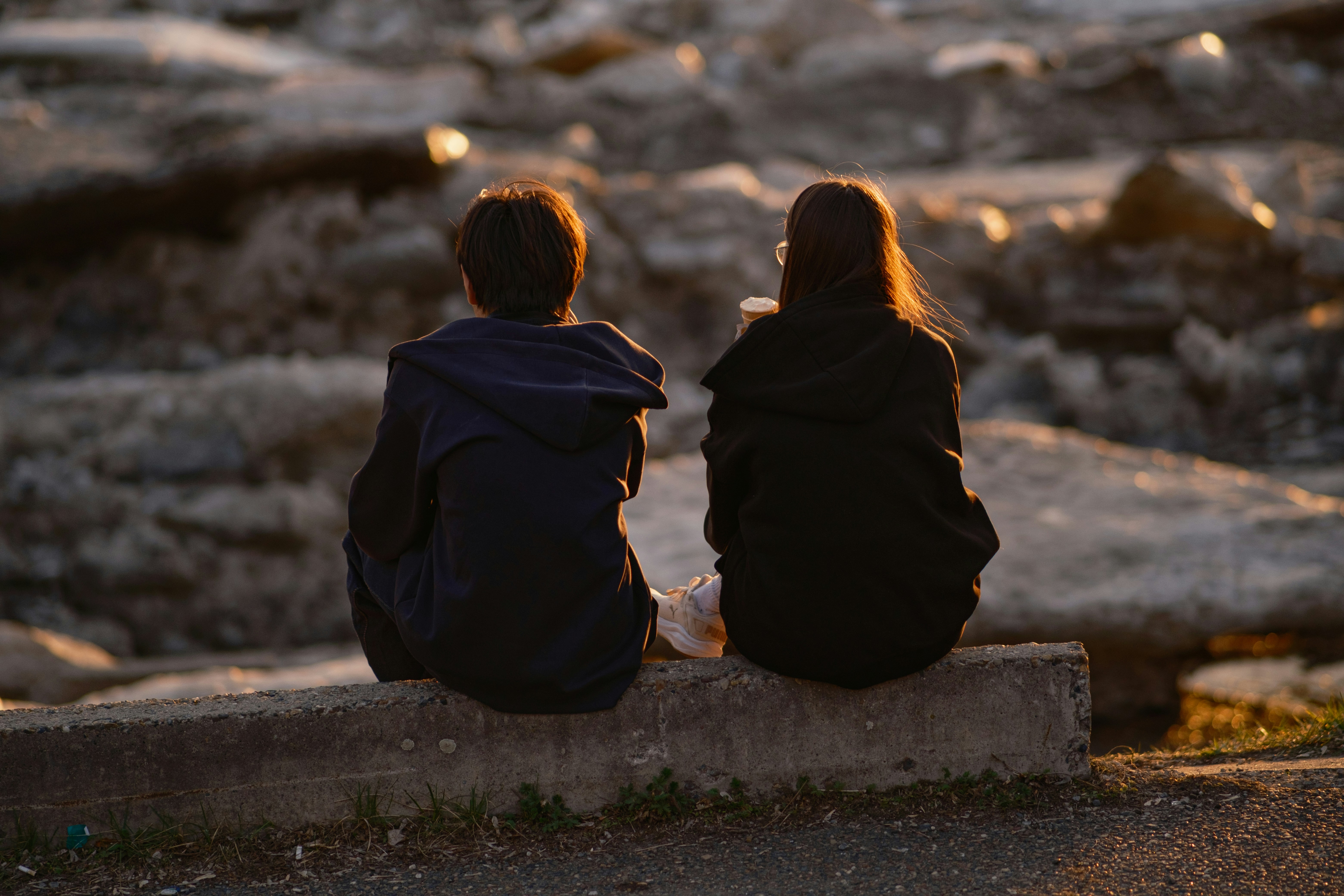 Two people sitting on a ledge at sunset