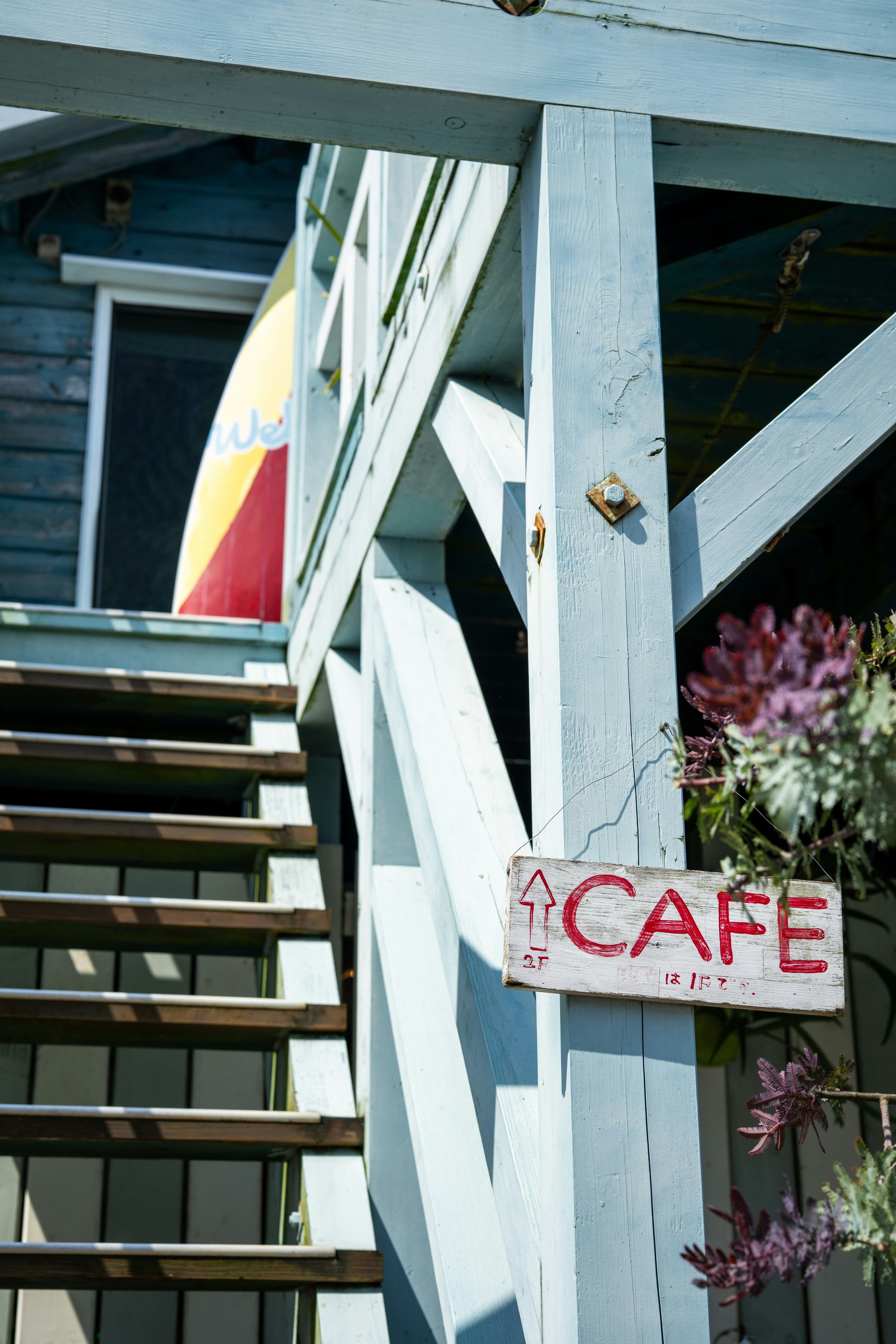Wooden stairs lead to a cafe with a surfboard.