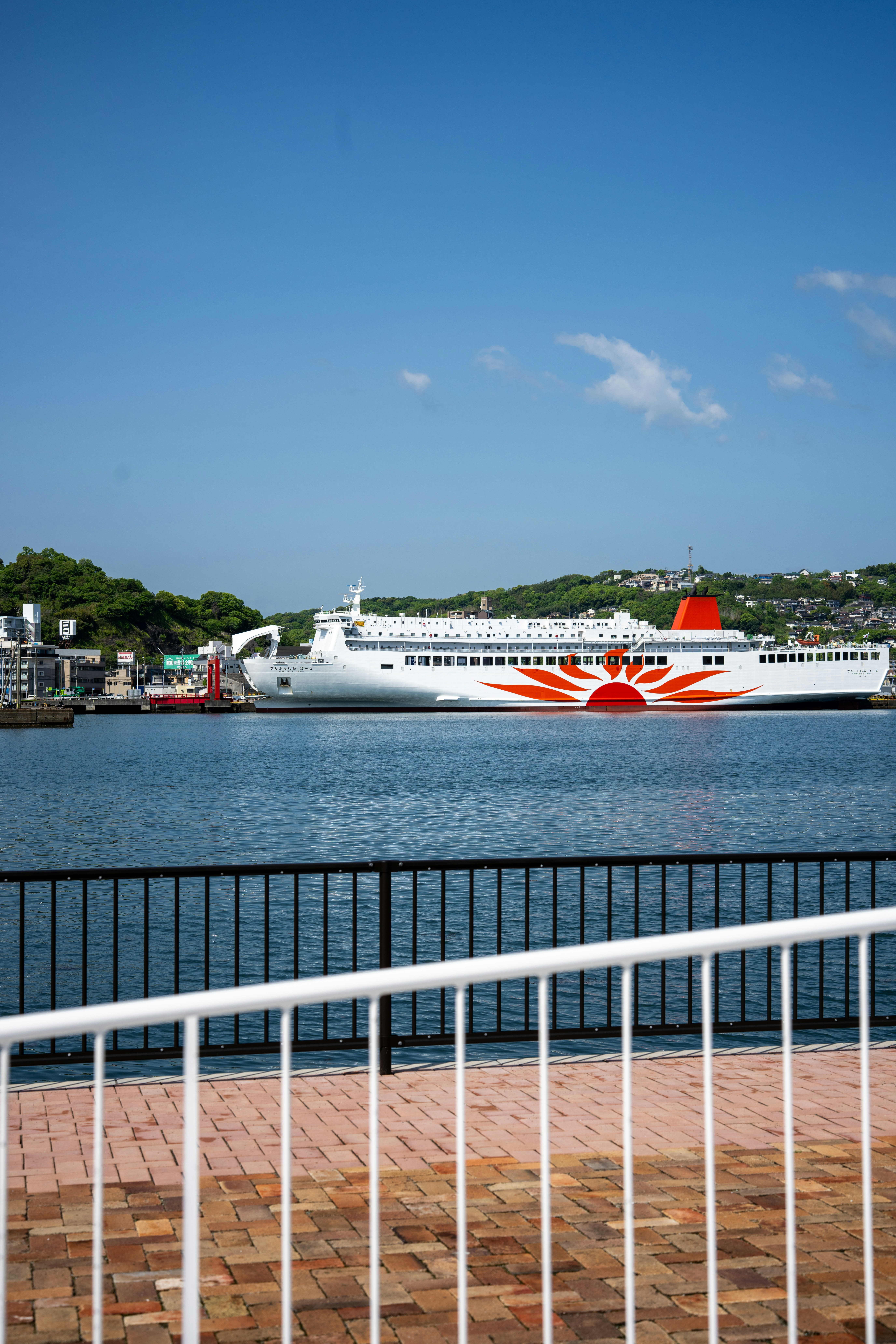 A large white ferry with a red sun logo docked.