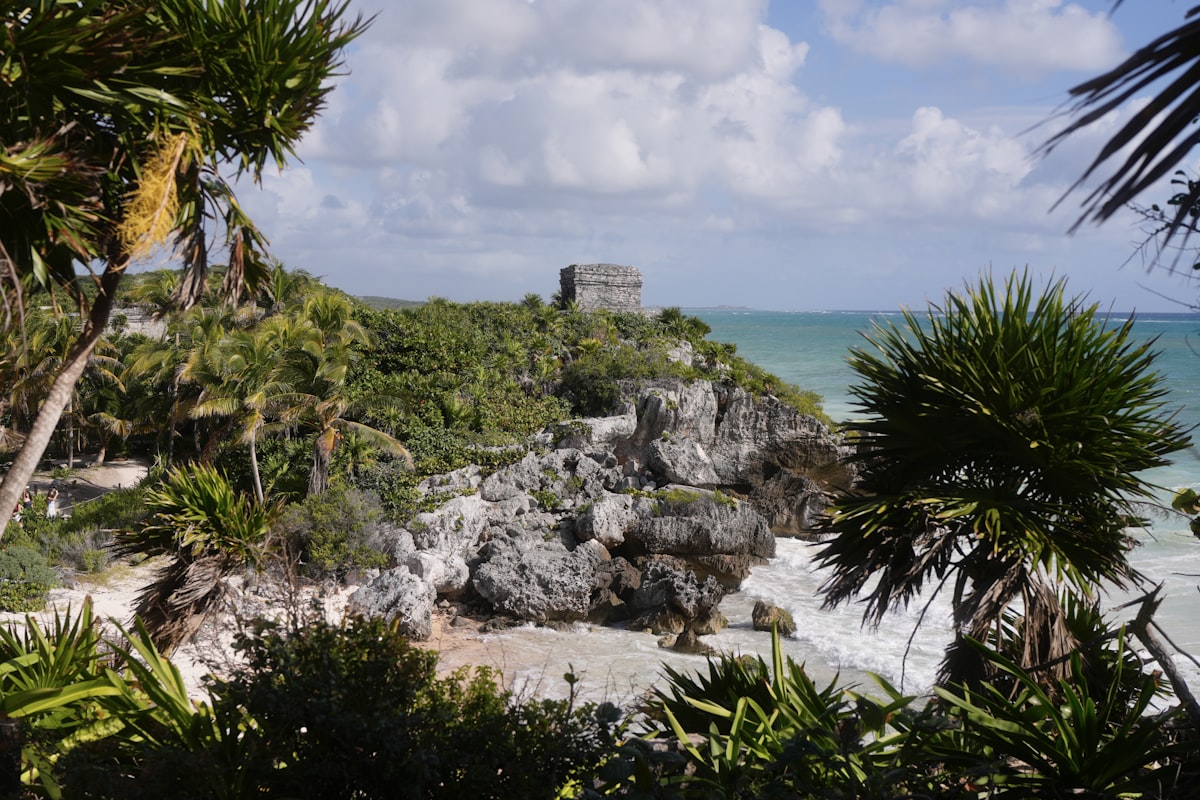 Tulum Mayan ruins on a limestone cliff above the turquoise Caribbean Sea, framed by tropical palms under a bright sky