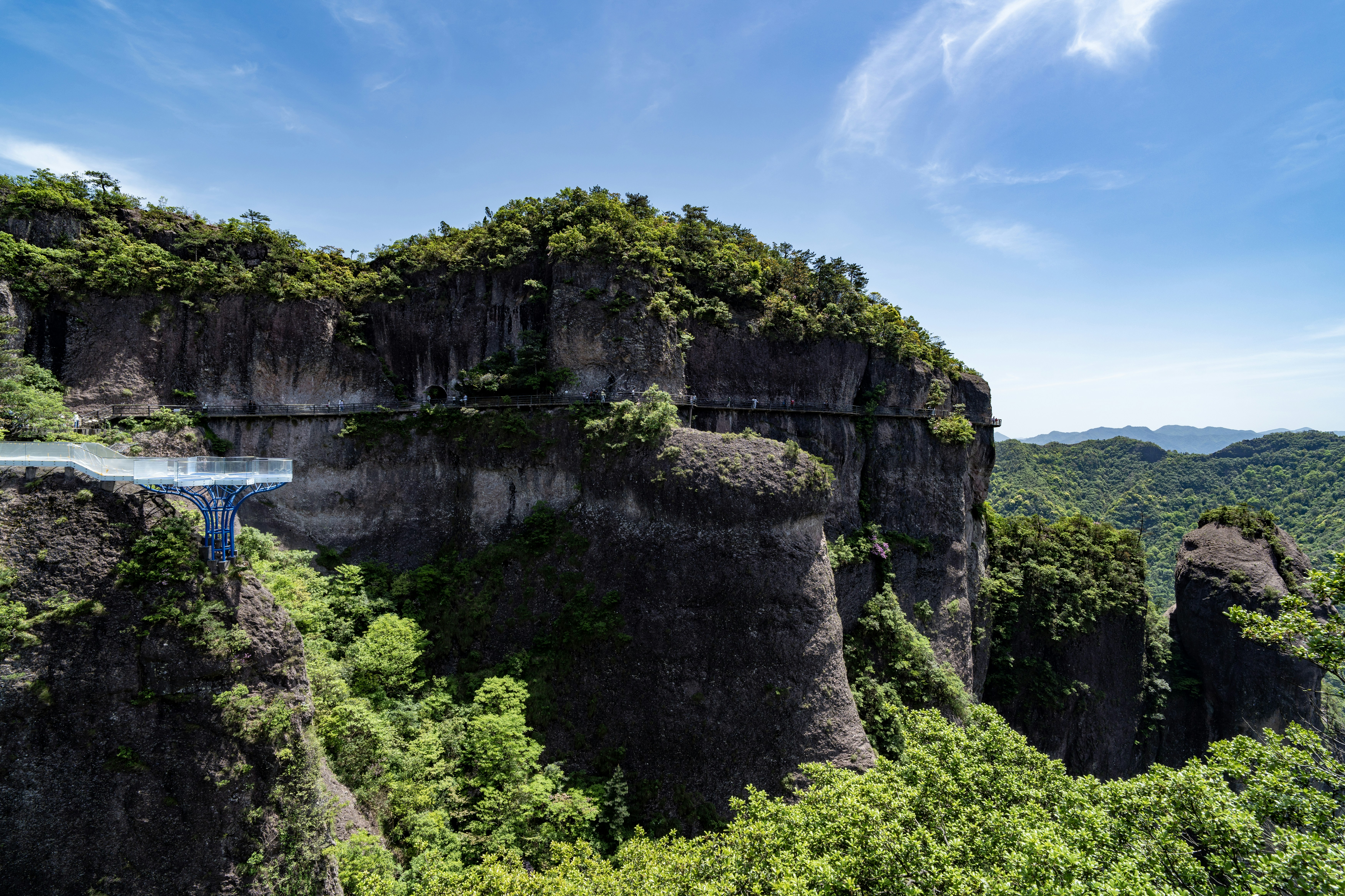 Glass walkway along a green cliffside above the sea