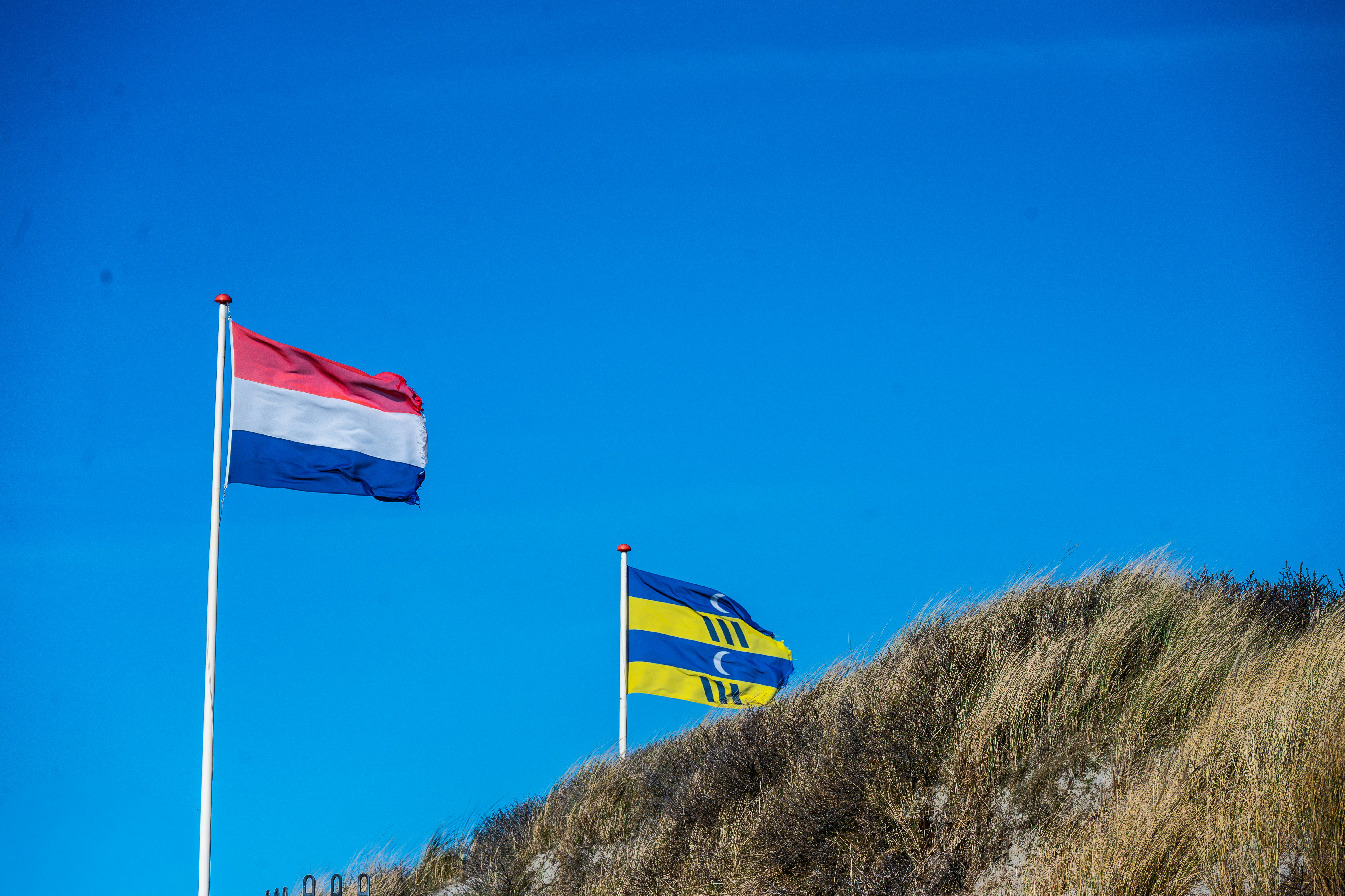 Deux drapeaux flottent sous un ciel bleu clair.